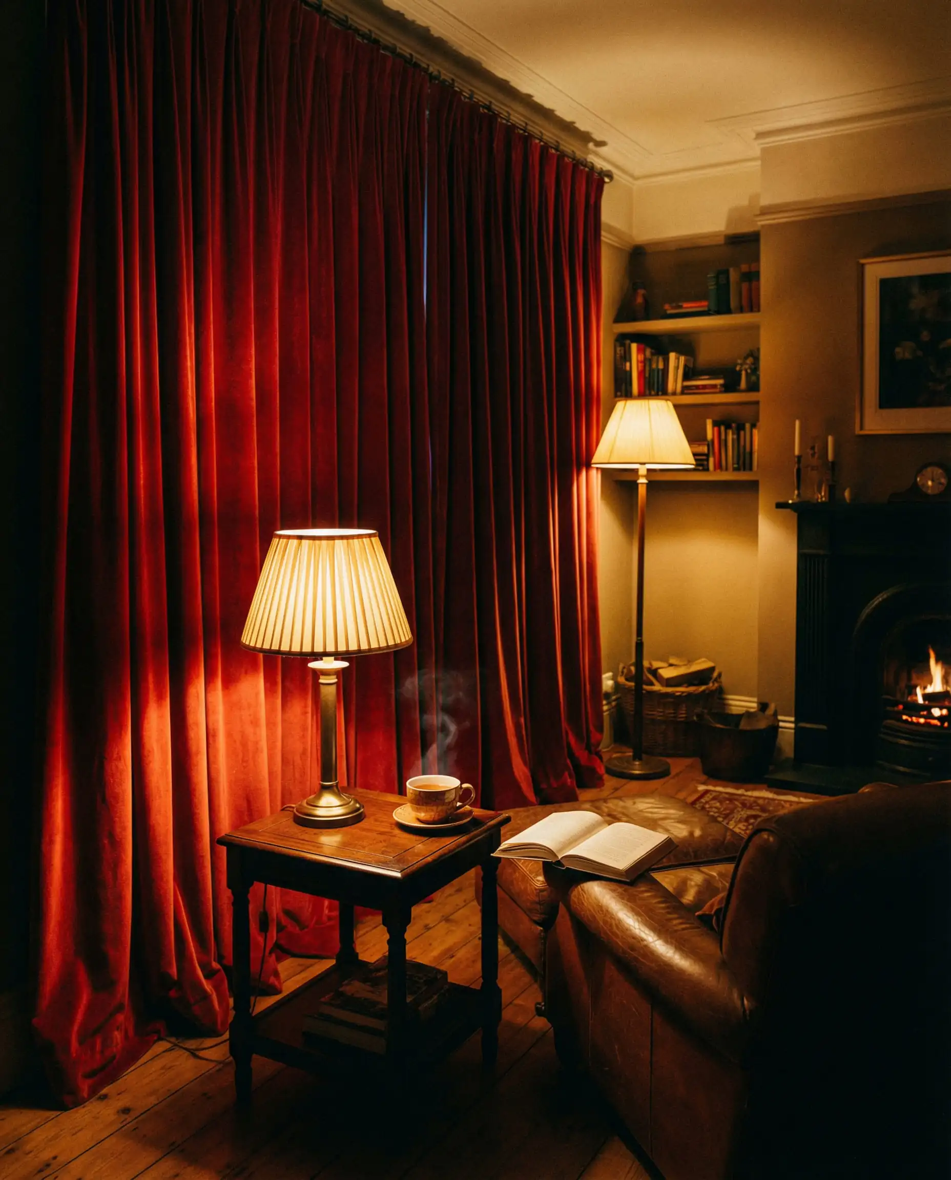 Living room at night with red velvet curtains drawn closed, lit by warm lamp light.