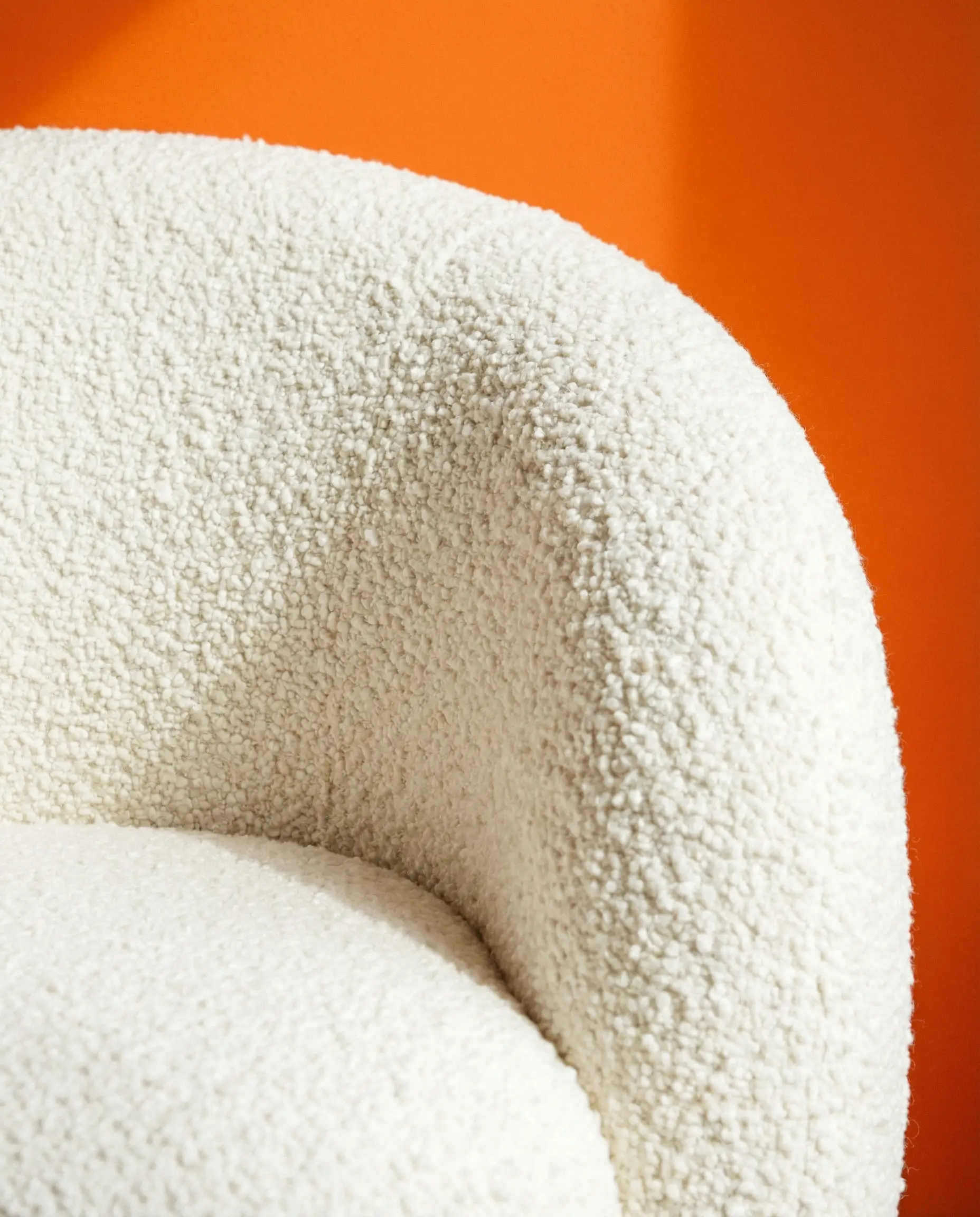 Detail shot of cream bouclé wool fabric on an armchair against a vibrant tangerine orange wall.