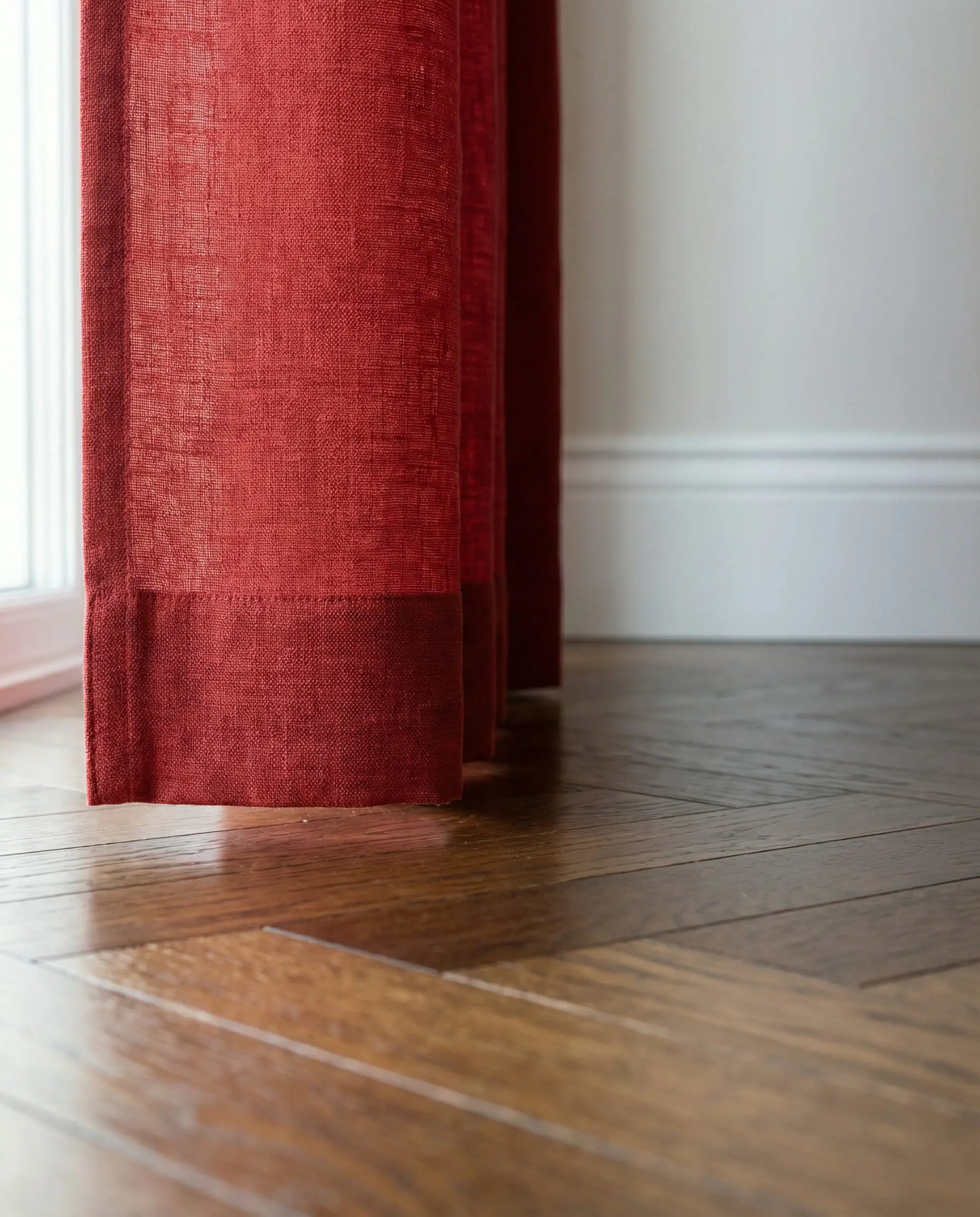 Detail shot of a red linen curtain hem hovering just above a hardwood floor.