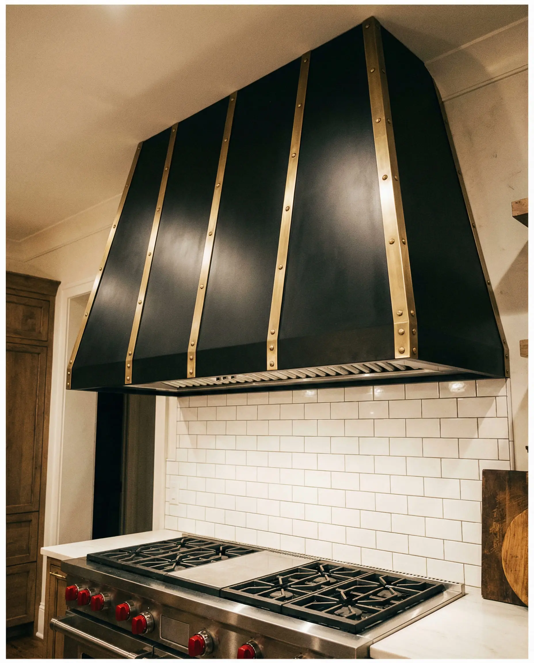 Large custom matte black range hood featuring vertical brushed brass straps and rivets.