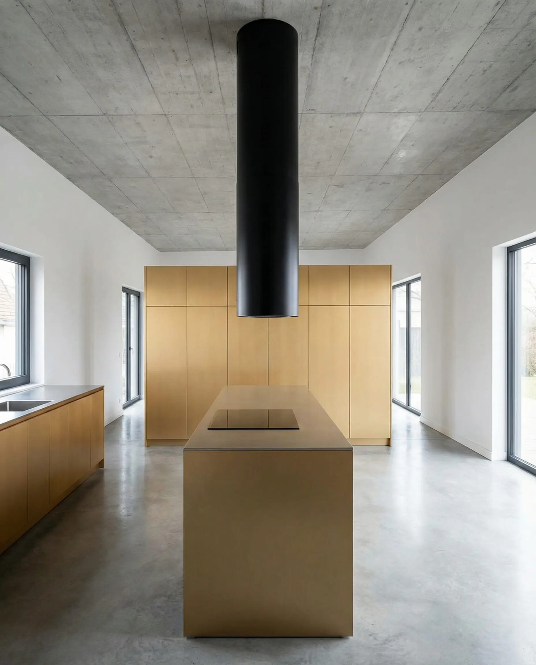Sleek cylindrical matte black range hood descending from the ceiling over a kitchen island.