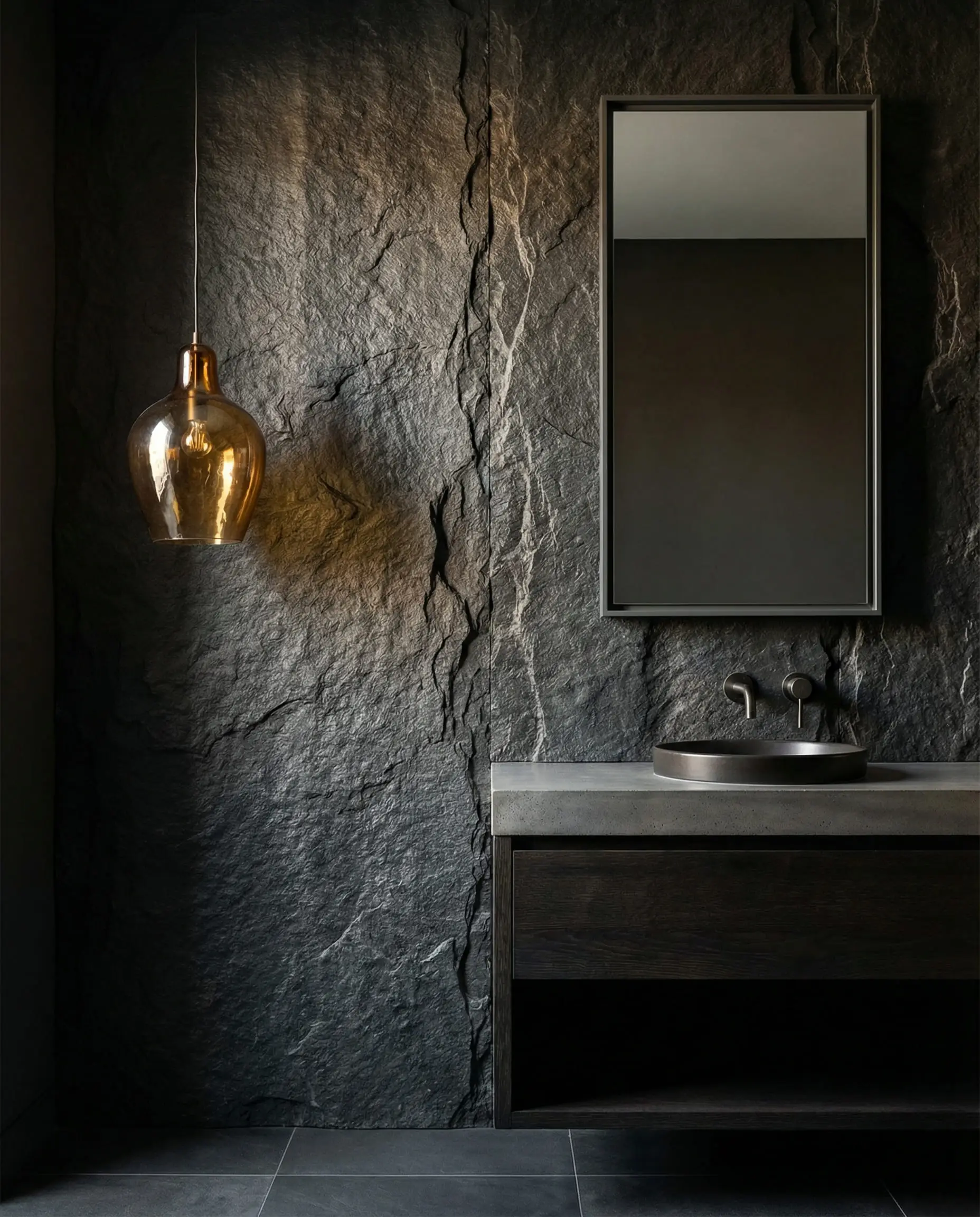 Asymmetrical bathroom vanity featuring a raw, dark grey slate stone wall with dramatic grazing lighting.