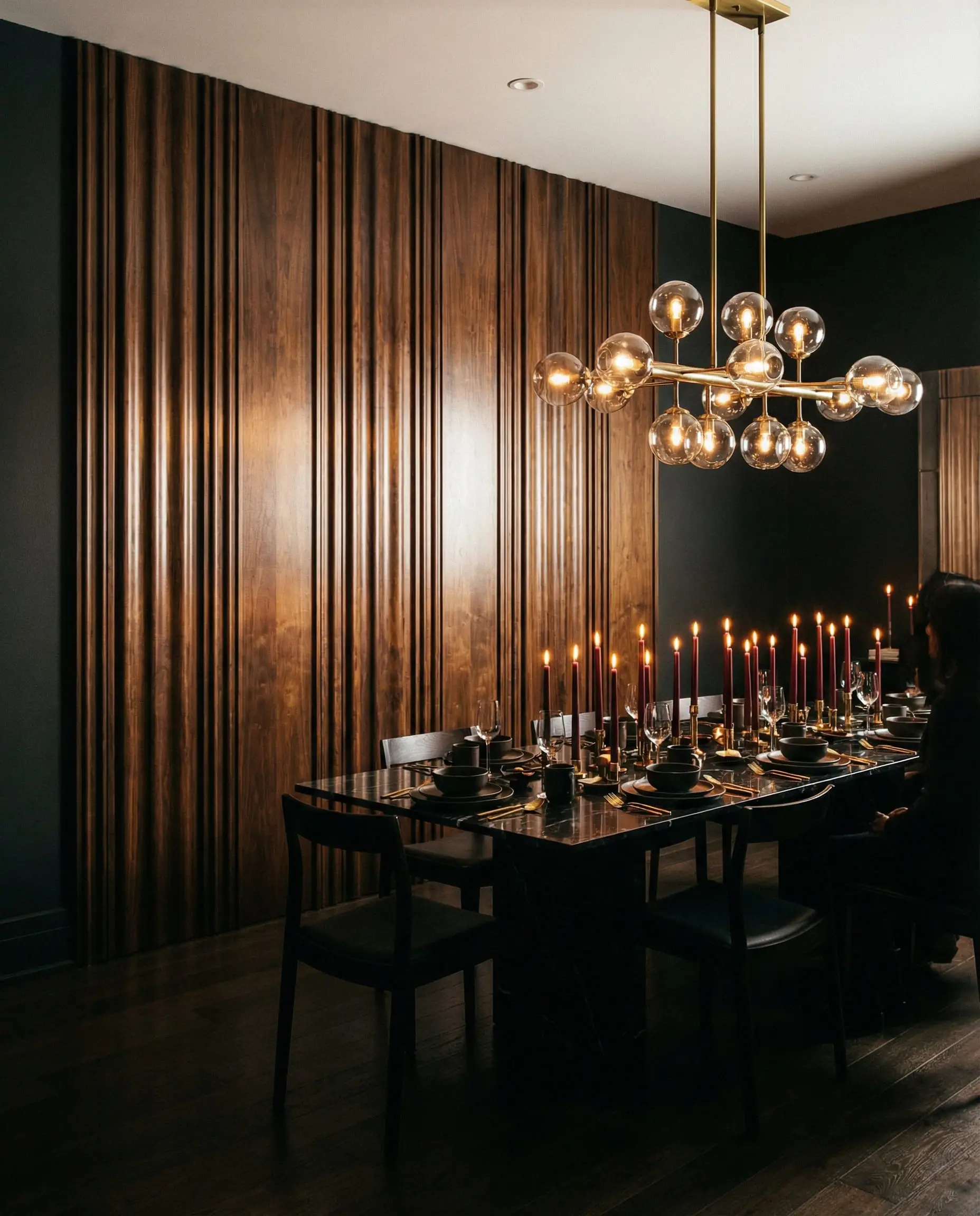 Formal dining room featuring rich dark walnut fluted wall paneling, a brass chandelier, and a black marble table for a moody aesthetic.