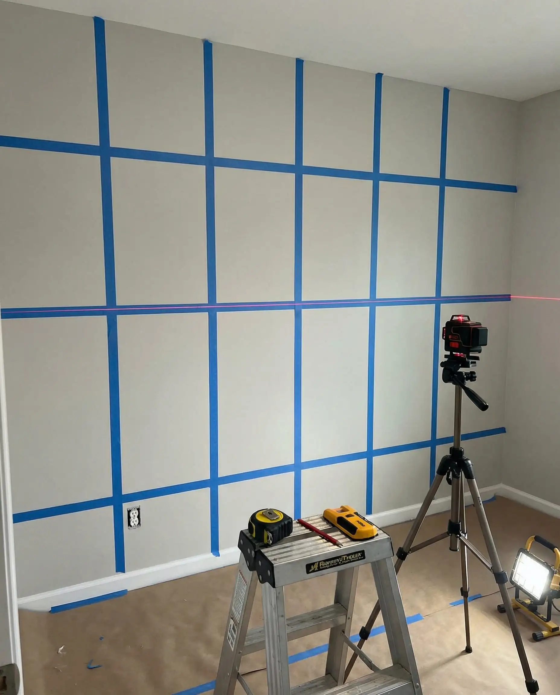 DIY scene showing a wall marked with blue tape and a red laser level line for batten installation.