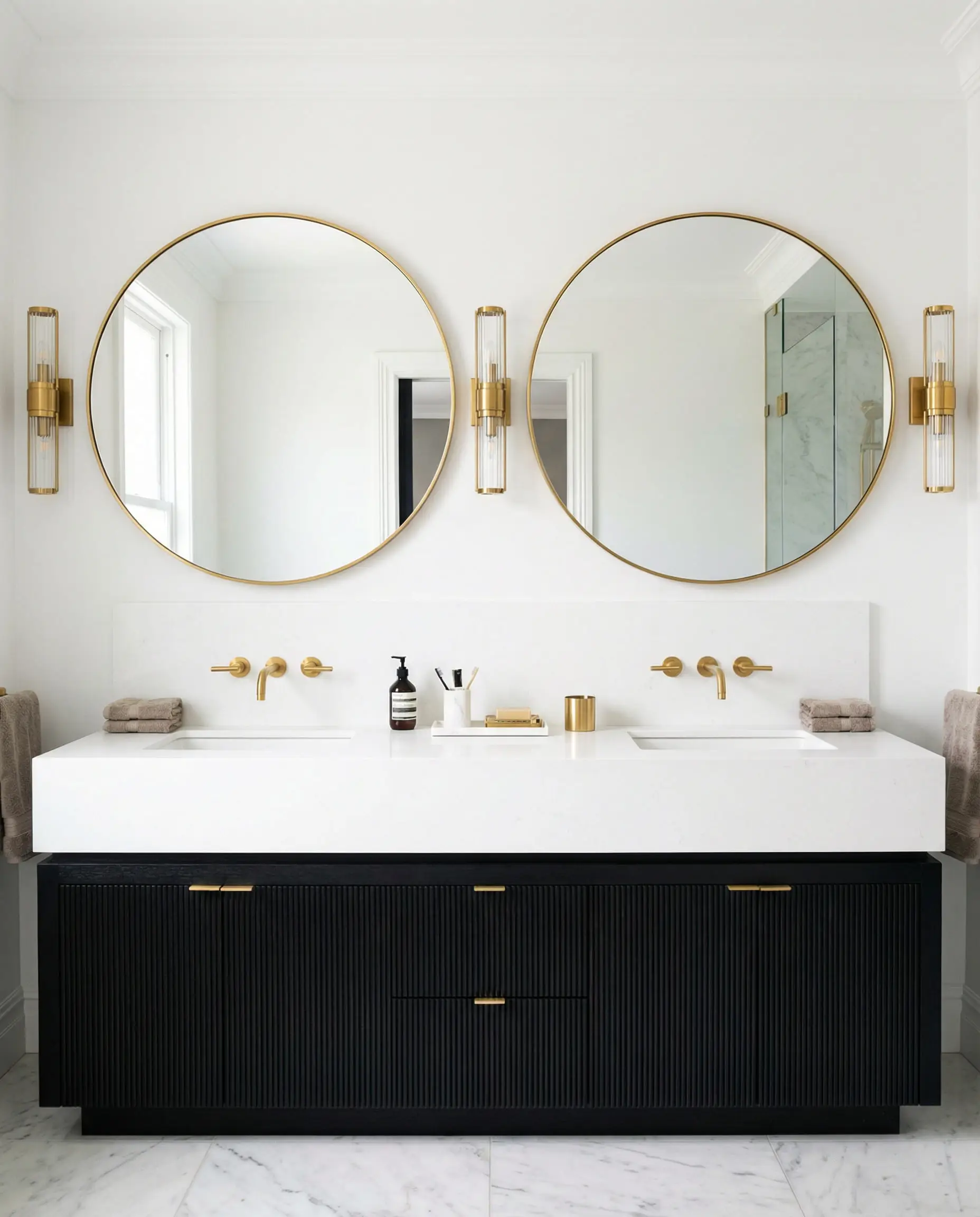 Symmetrical bathroom vanity in black wood with oversized round gold mirrors.