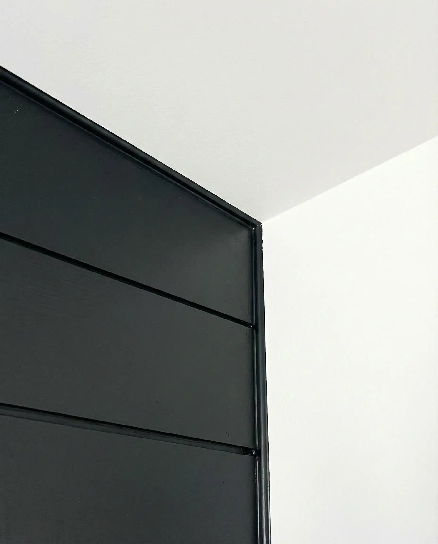 Detail of a perfectly caulked and painted corner of a black shiplap wall.