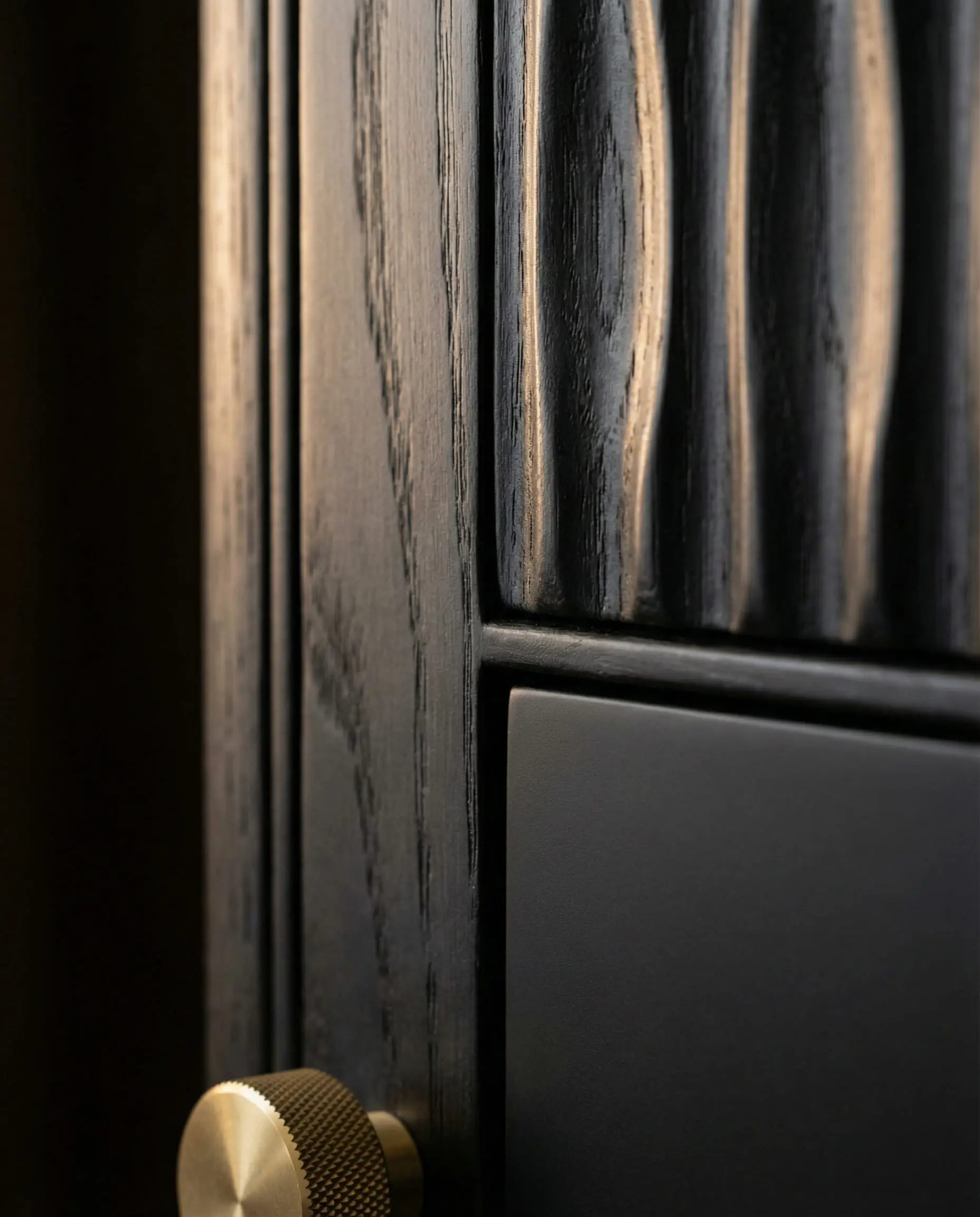 Macro close-up of fluted black wood cabinet texture meeting a smooth drawer front with a gold knob.