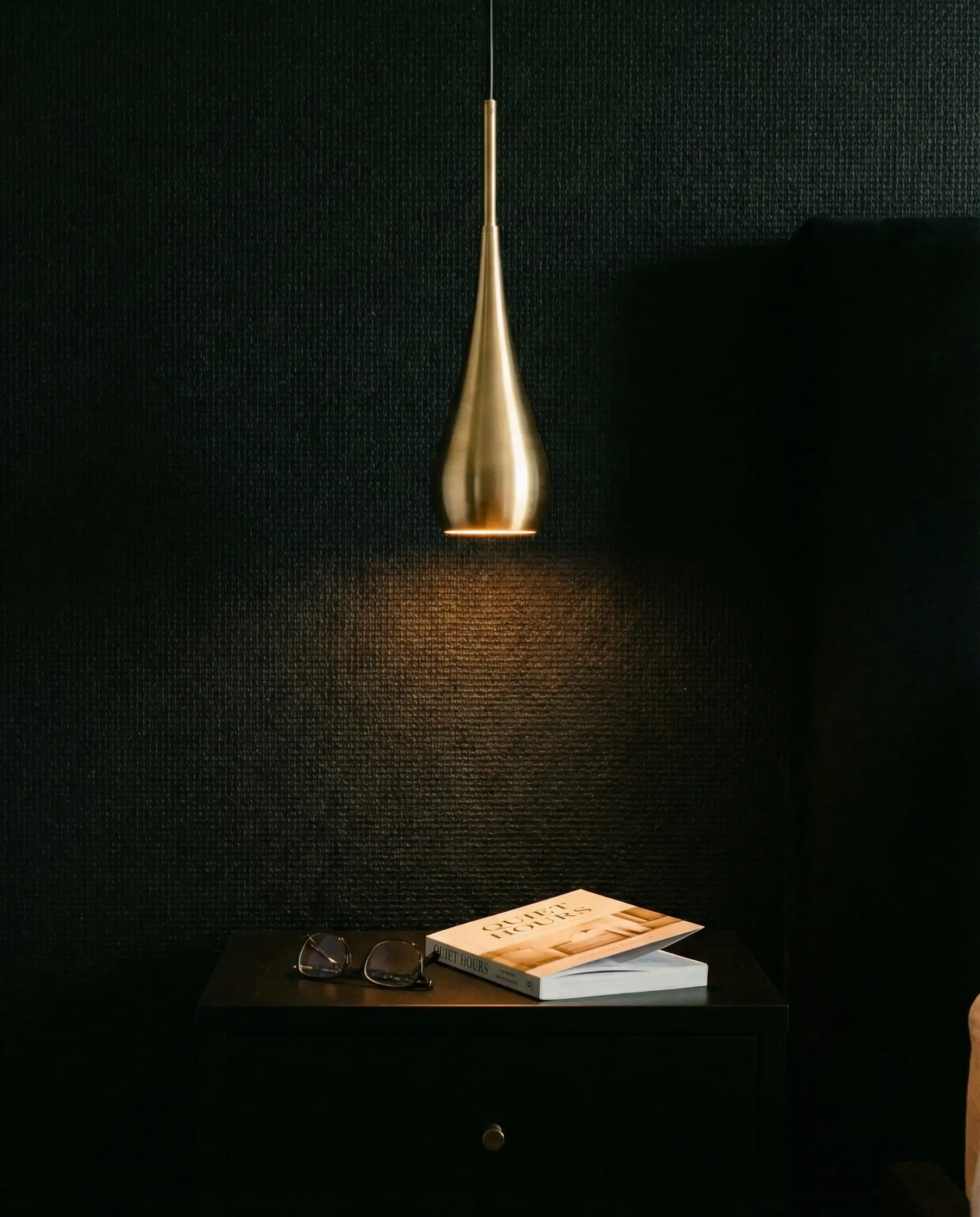 Atmospheric bedroom shot showing a gold teardrop pendant light against a black wall.