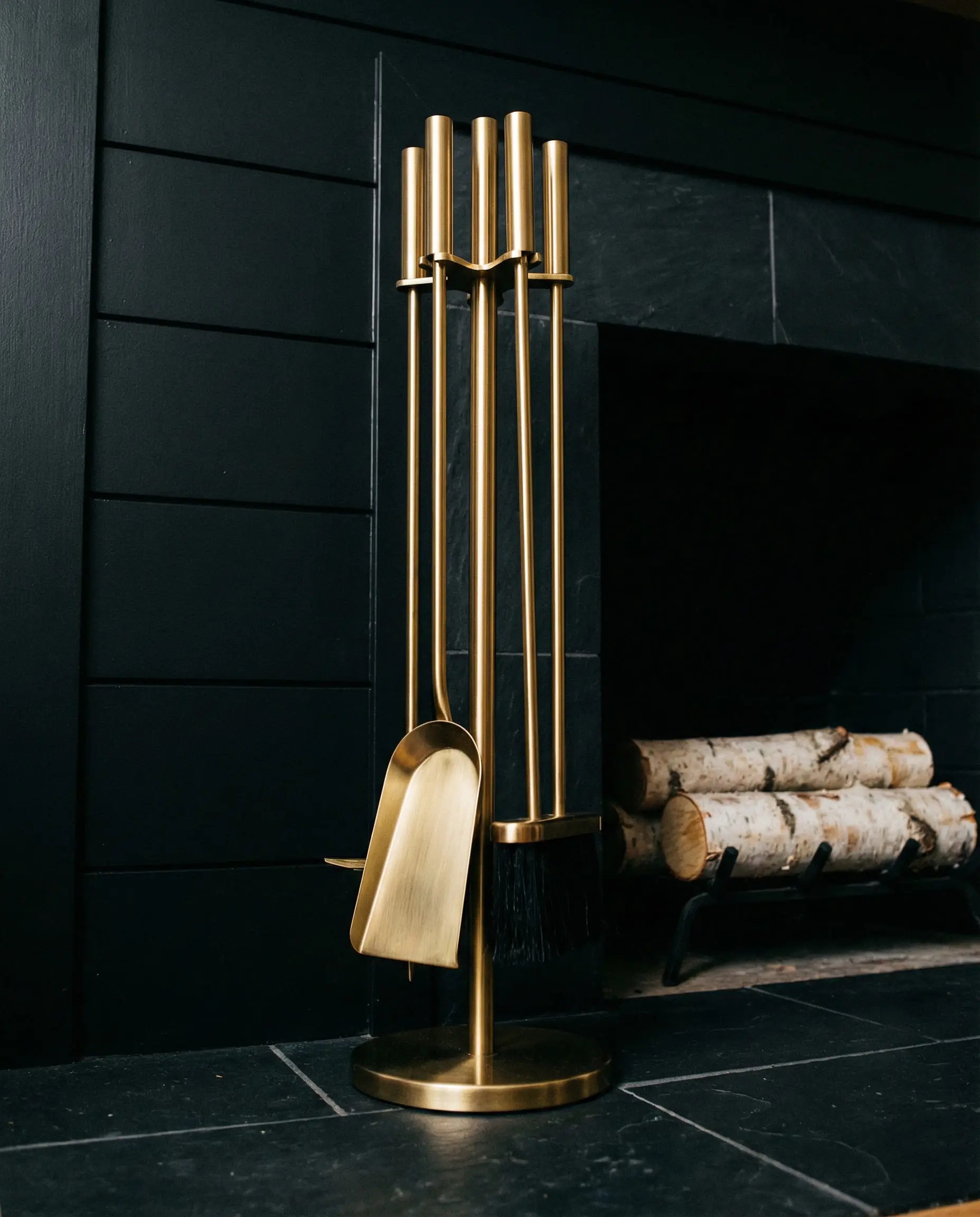 Modern brushed gold fireplace tools standing on a black slate hearth.
