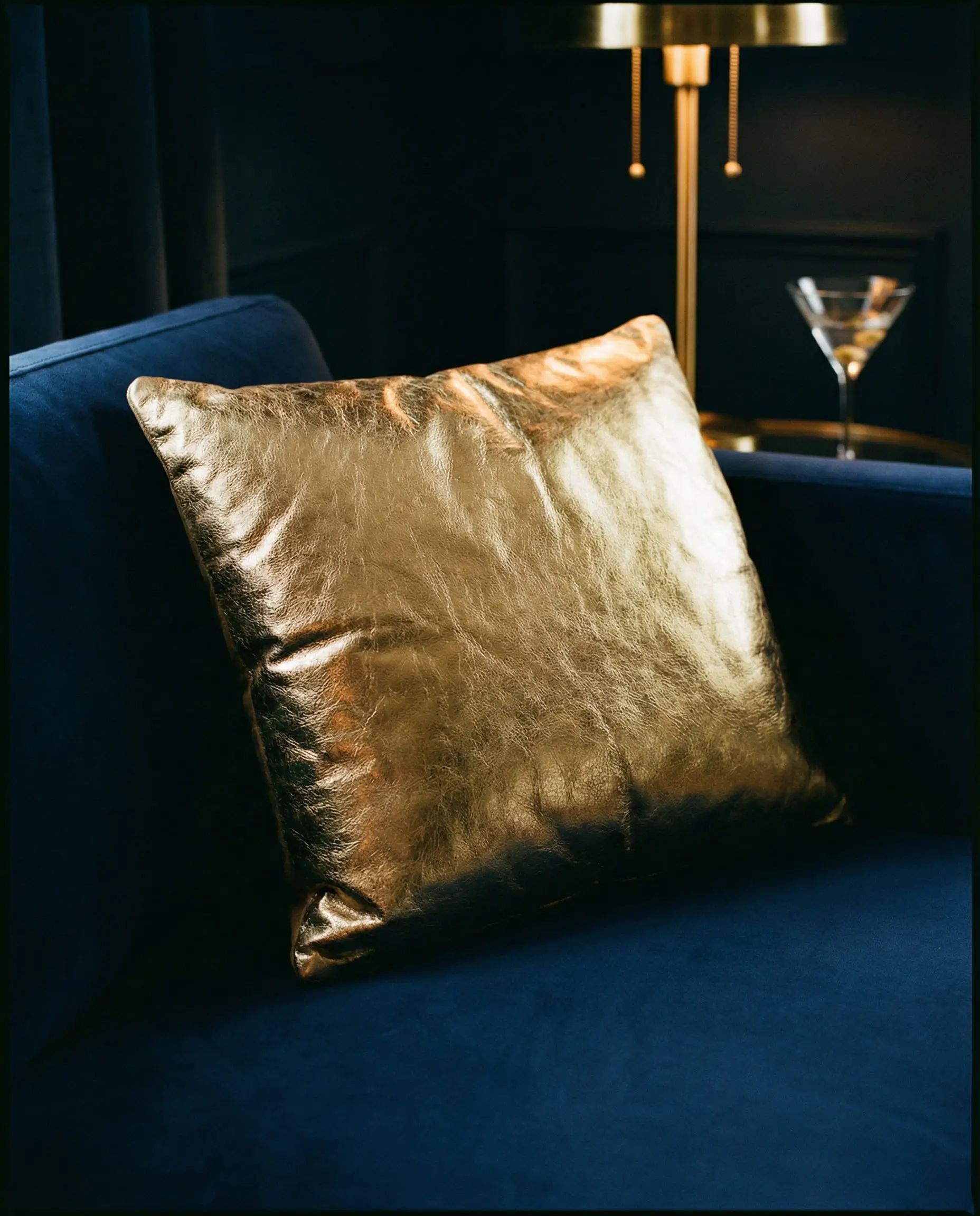 Metallic gold leather pillow on a matte navy blue sofa.