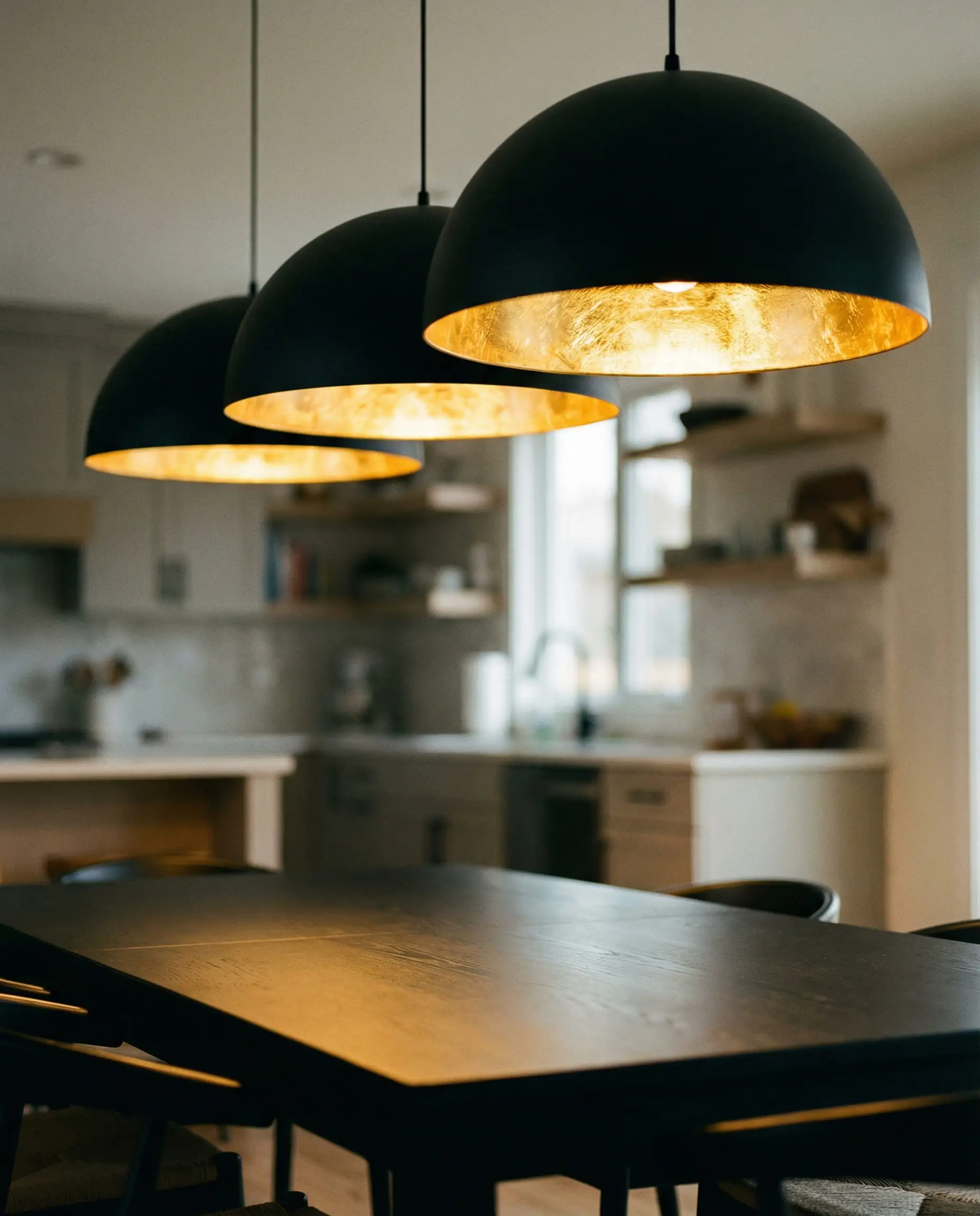 Trio of oversized black and gold pendant lights hanging over a kitchen dining table.