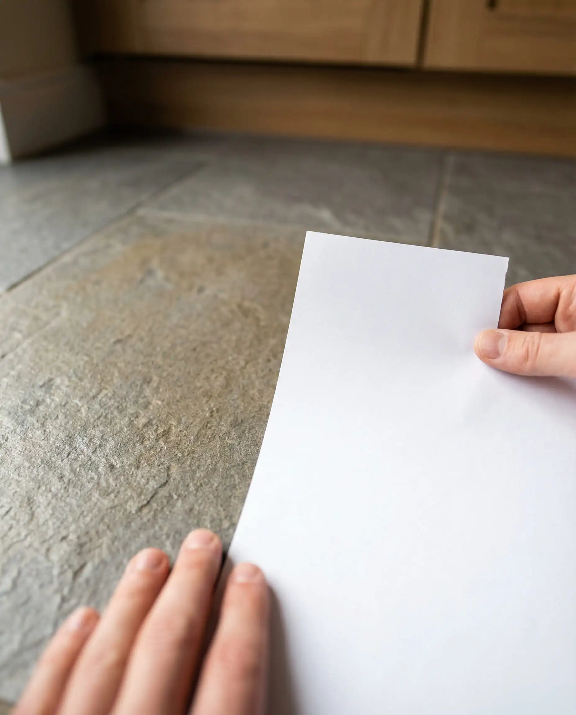 Hand holding a white sheet of paper against a gray floor tile to reveal muddy yellow-brown warm undertones.