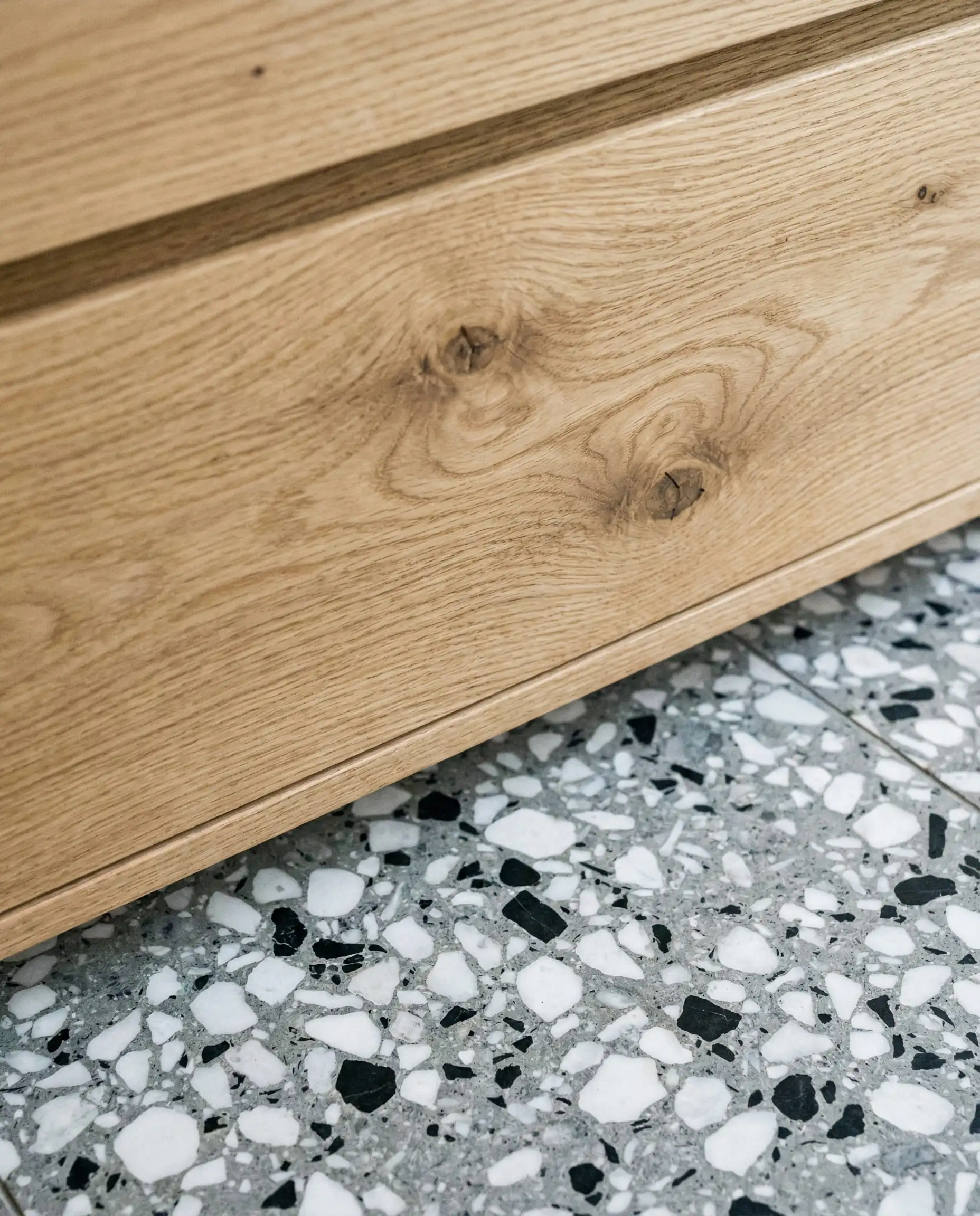Macro shot of natural oak wood grain texture meeting a gray terrazzo floor with aggregate.