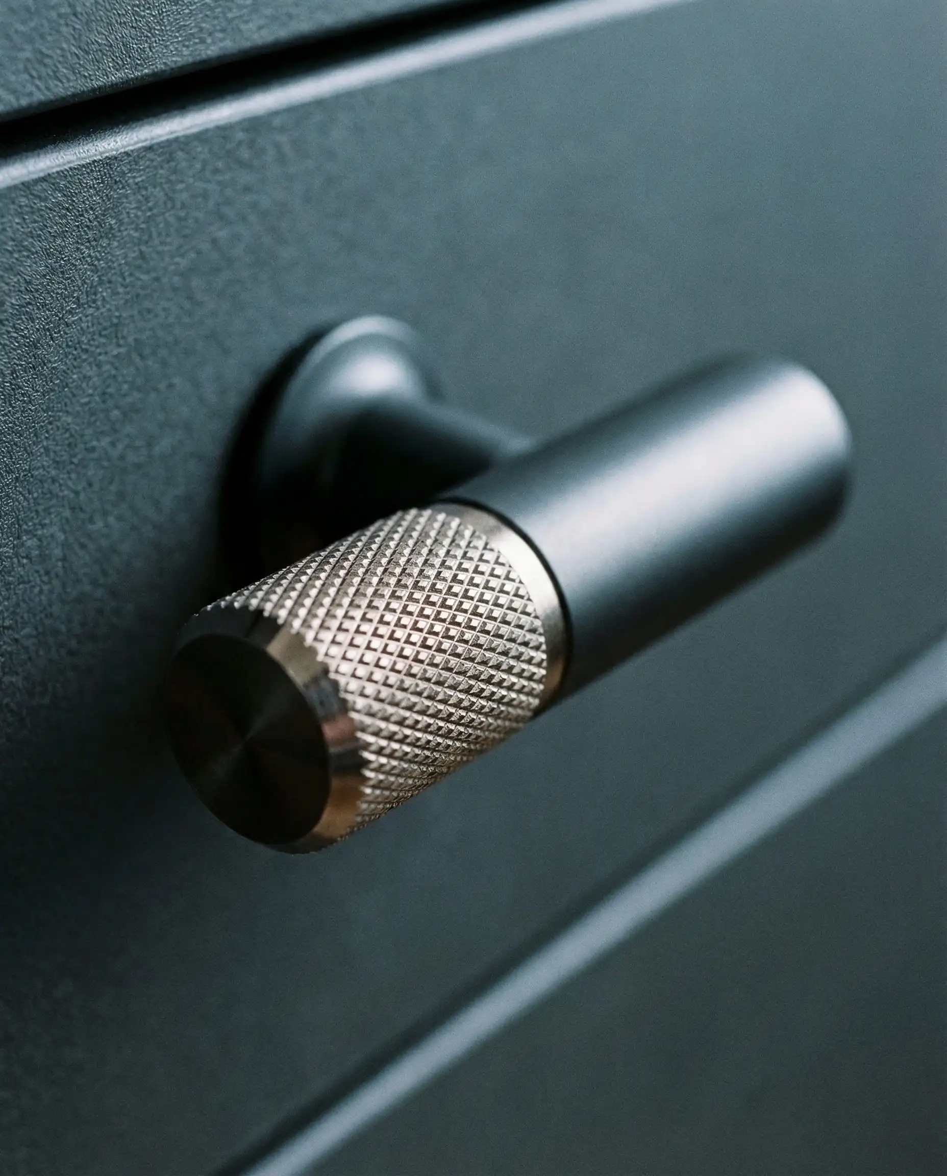 Macro shot of a knurled brass T-bar cabinet pull on a graphite grey cabinet door.