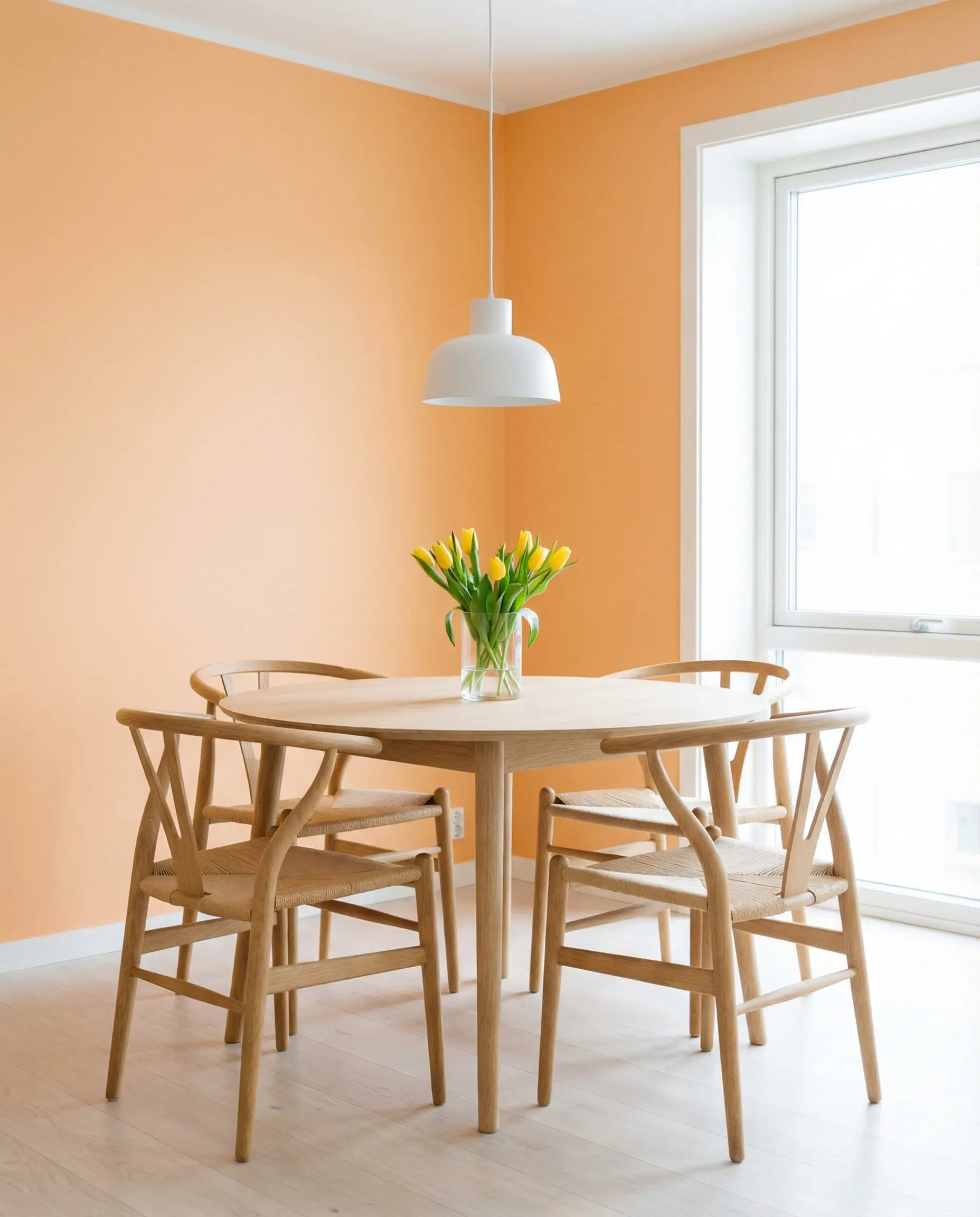 Bright Scandinavian dining nook with a light oak table and wishbone chairs against soft apricot orange walls.