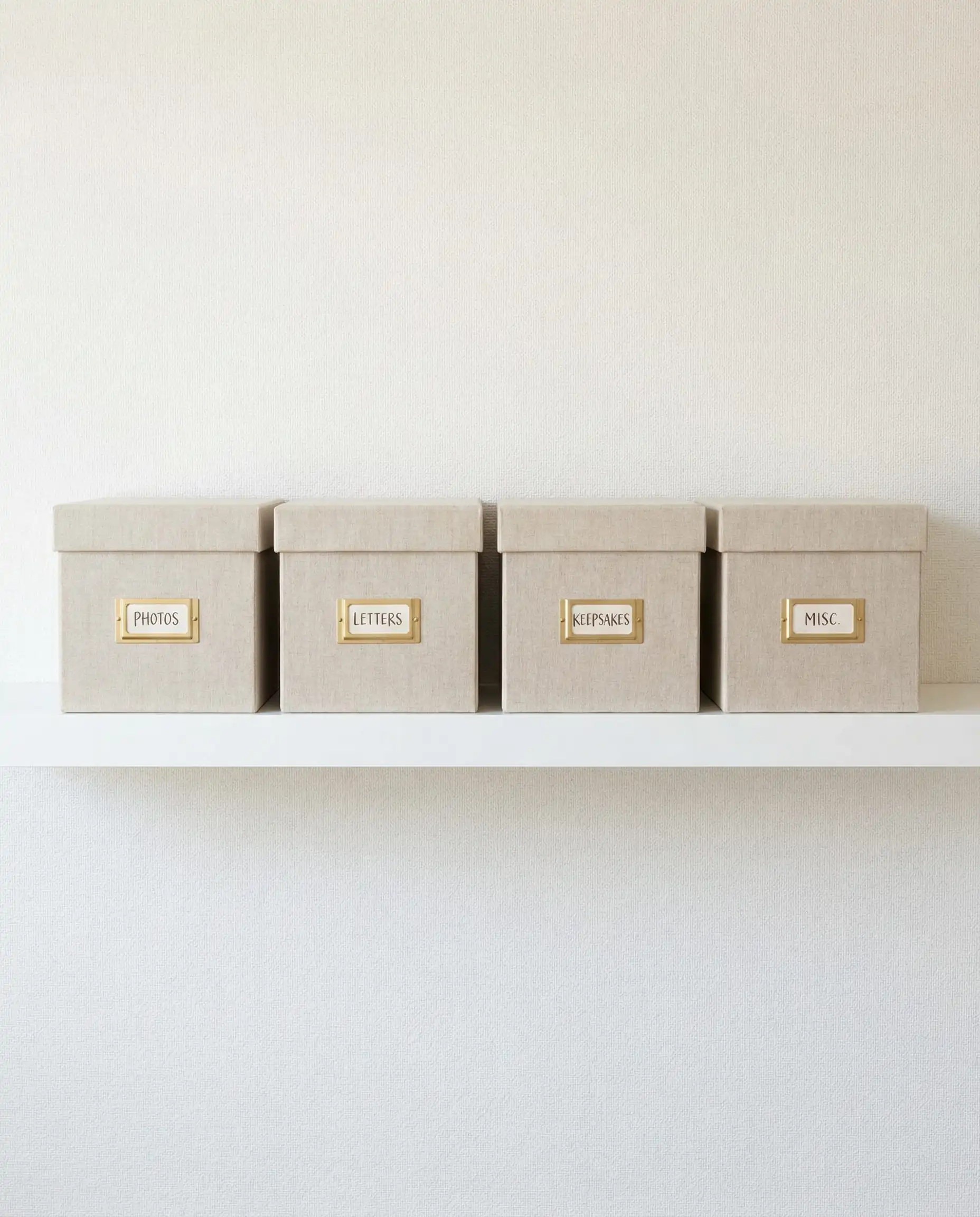Row of uniform beige linen storage boxes with labels on a white floating shelf.