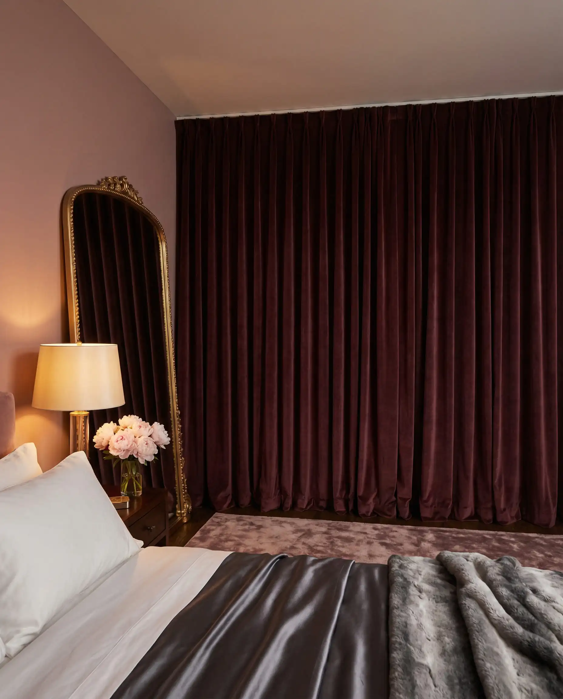 Luxurious bedroom with floor-to-ceiling burgundy velvet drapes, a gold mirror, and hotel-style bedding.