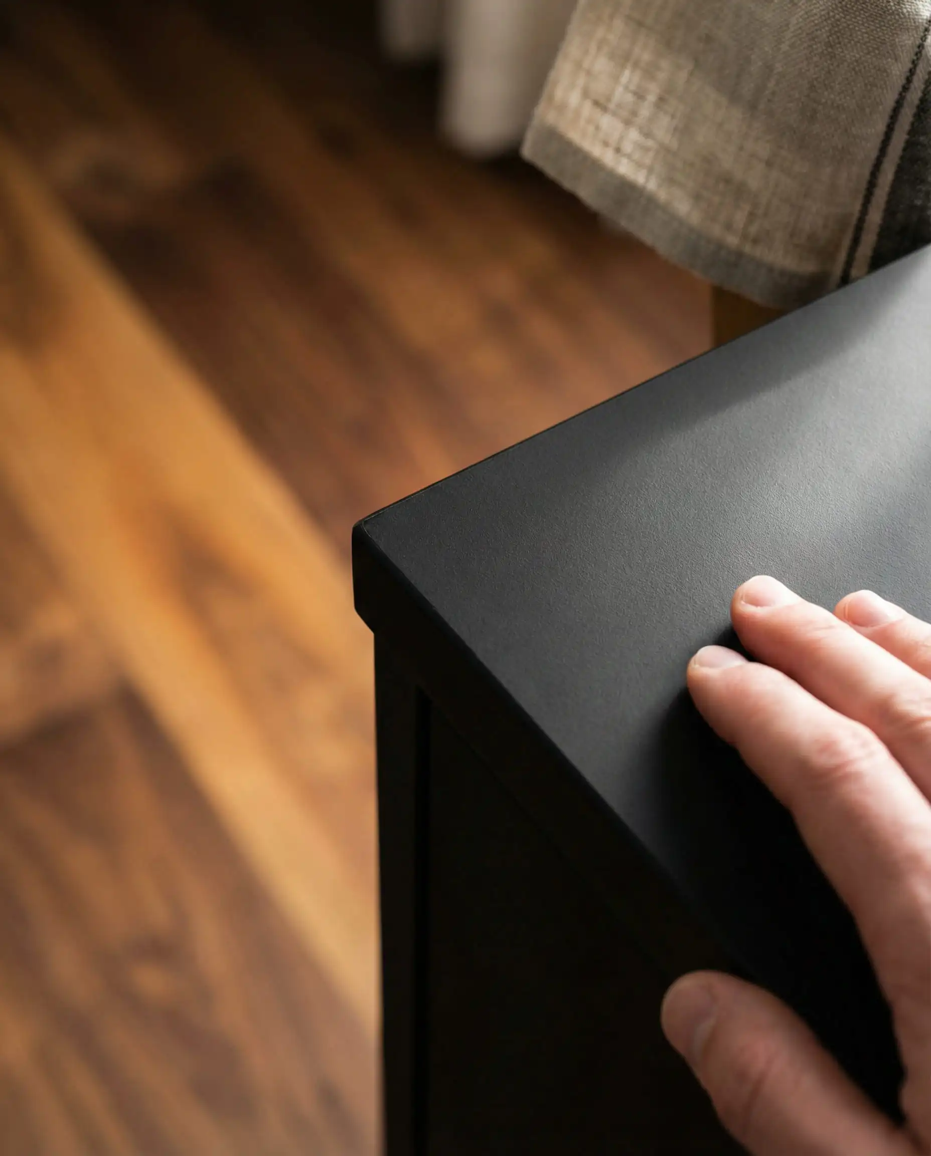 Close-up of Fenix matte black kitchen cabinet material showing zero reflection and anti-fingerprint texture against a walnut floor background.
