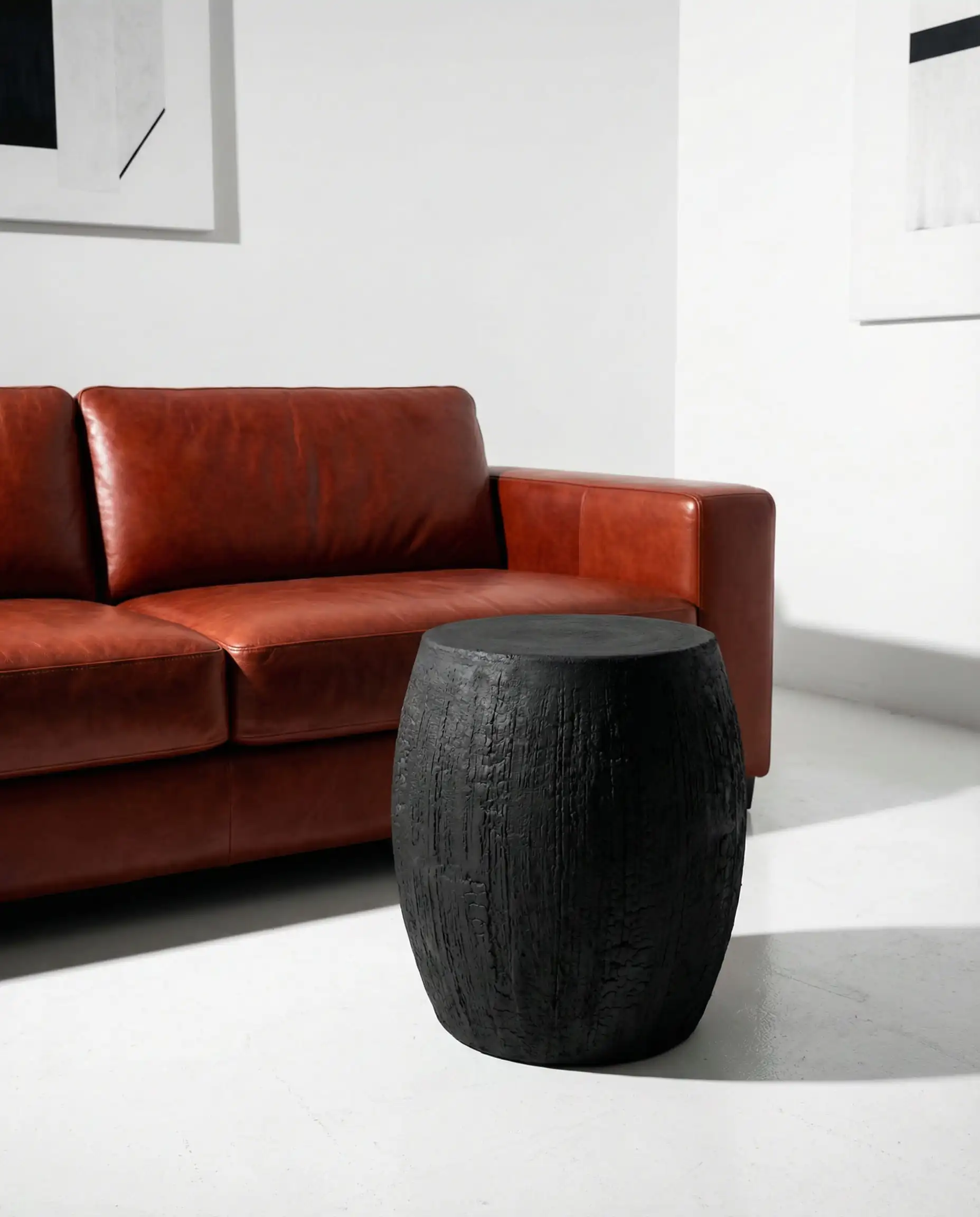 Sculptural matte black charcoal ceramic coffee table providing high contrast against a reddish-tone cognac leather sofa in a white room.