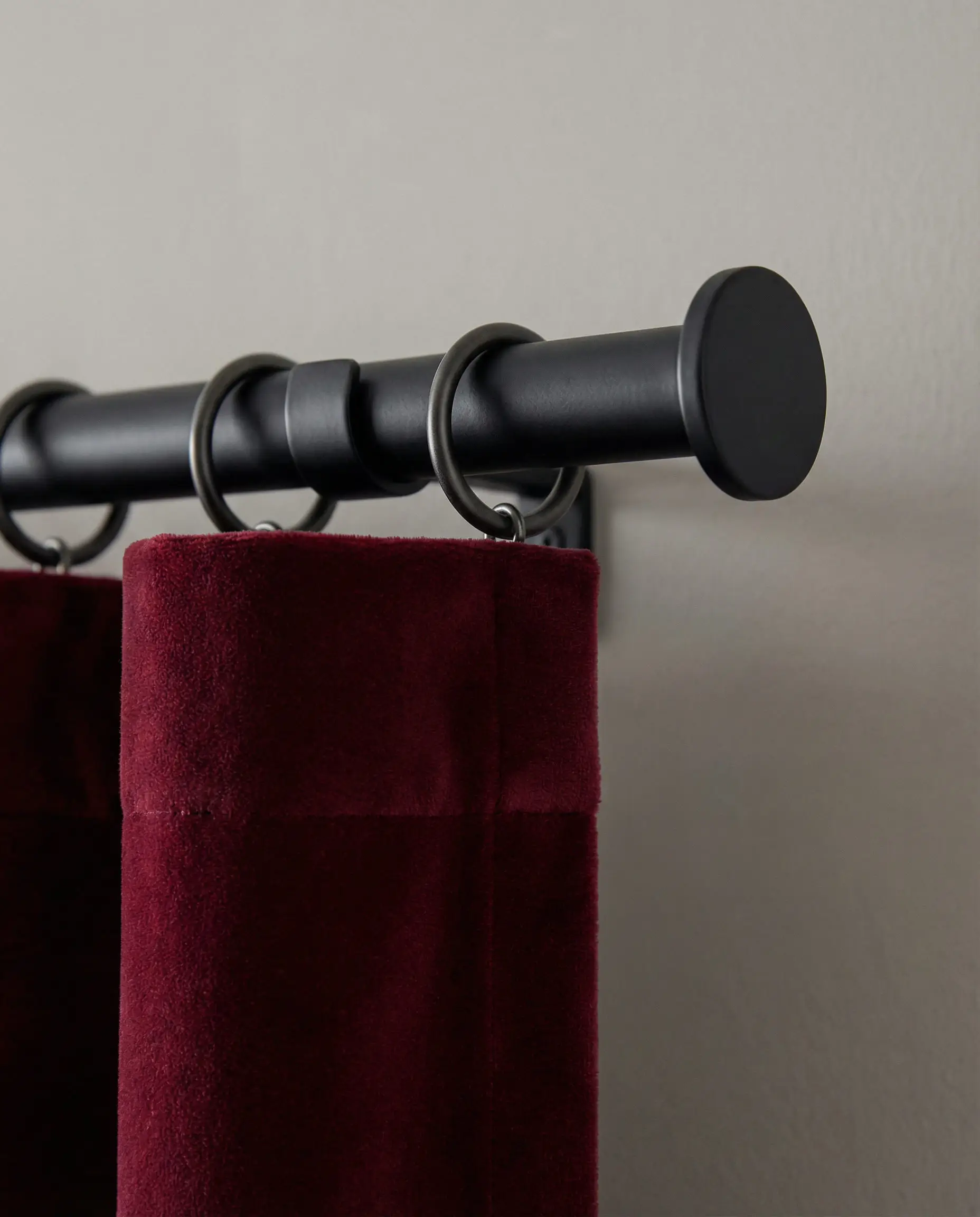 Close-up of matte black curtain rings and rod holding a burgundy velvet curtain panel.