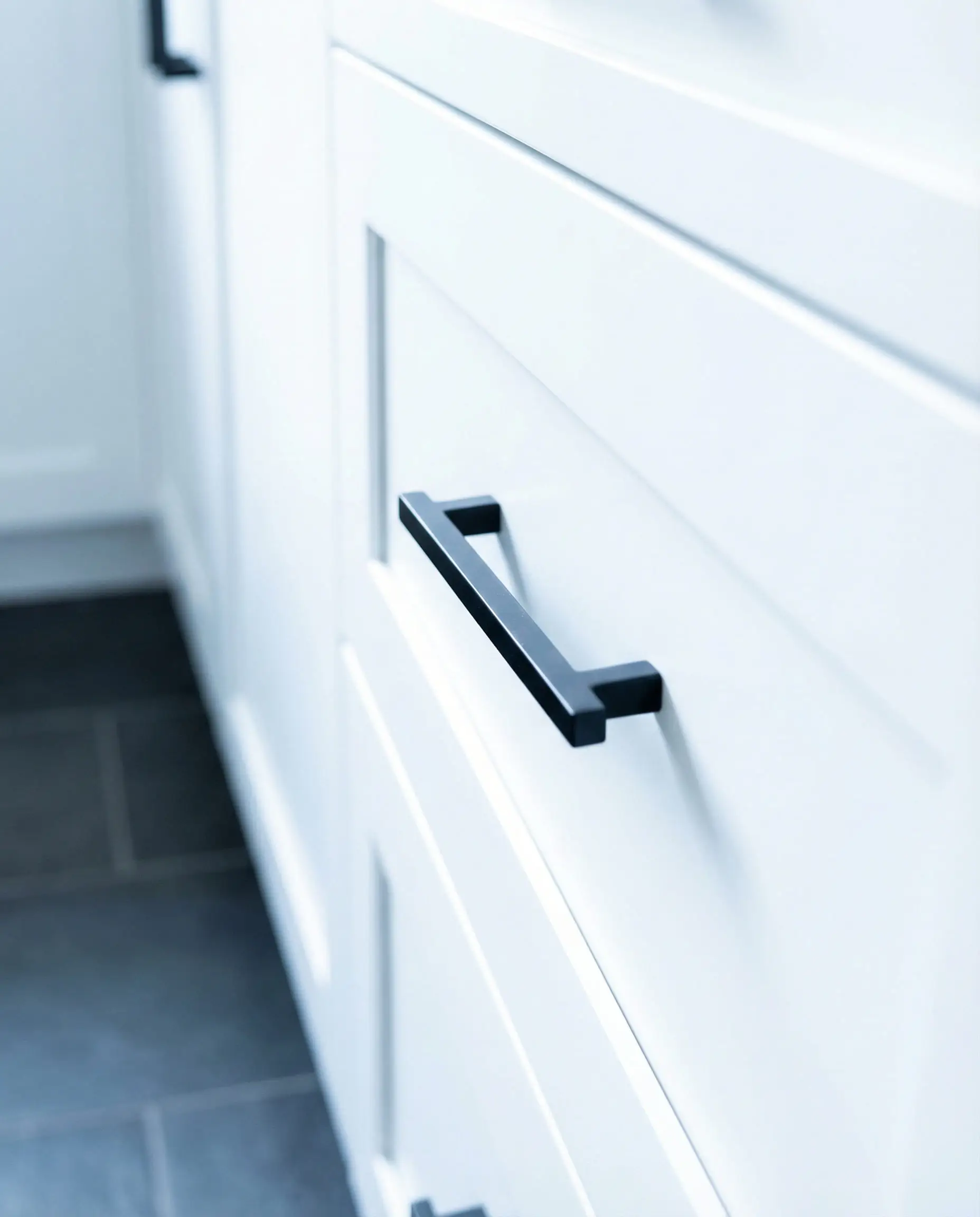 Sleek matte black handle on a white shaker cabinet drawer.