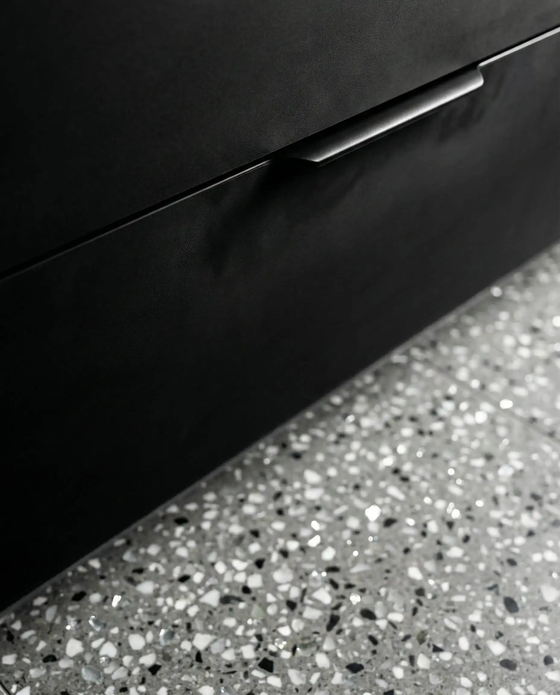 Macro detail of fingerprint-resistant matte black cabinet finish against a gray terrazzo floor.