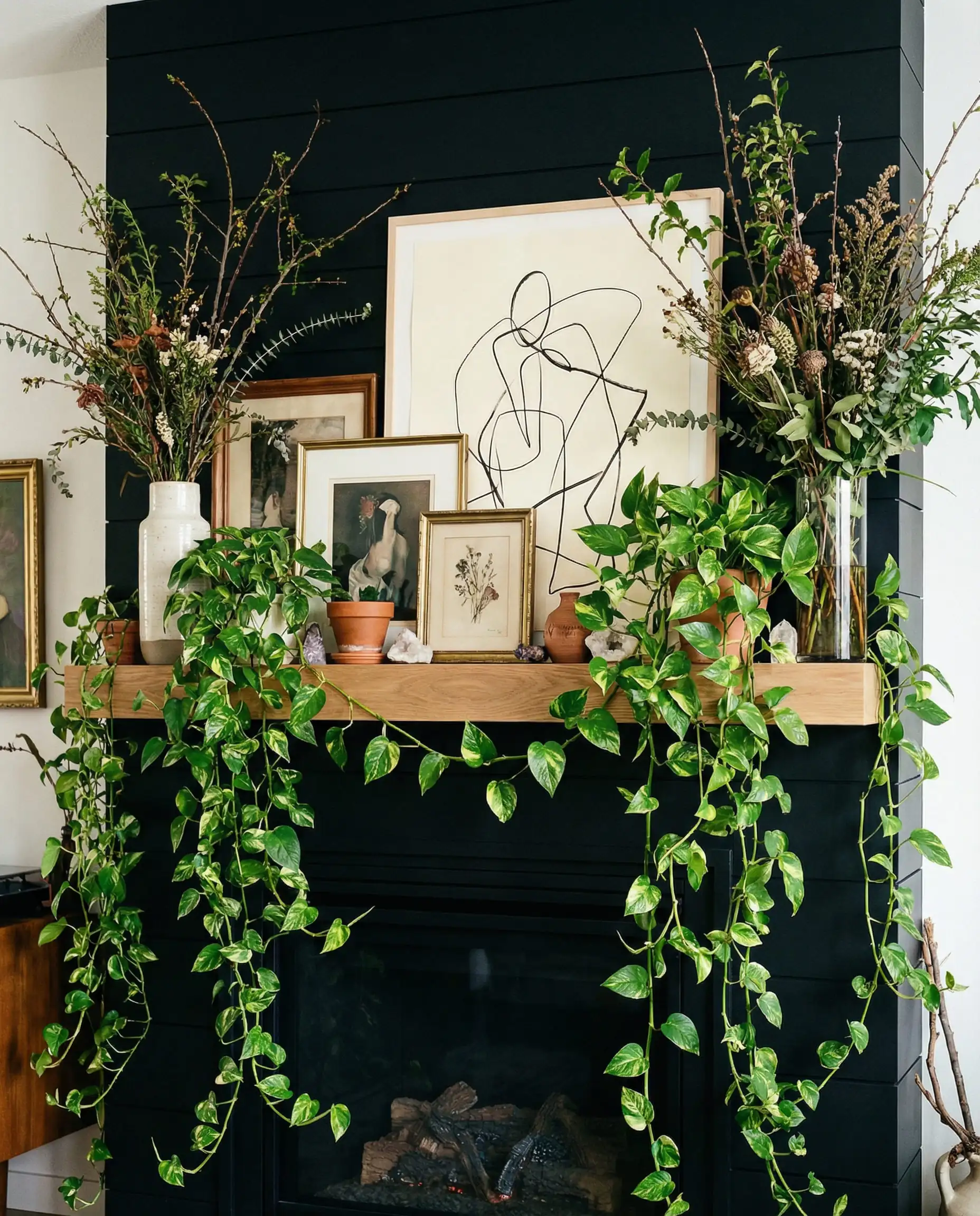 Black shiplap fireplace with oak mantel styled with cascading plants and layered art.