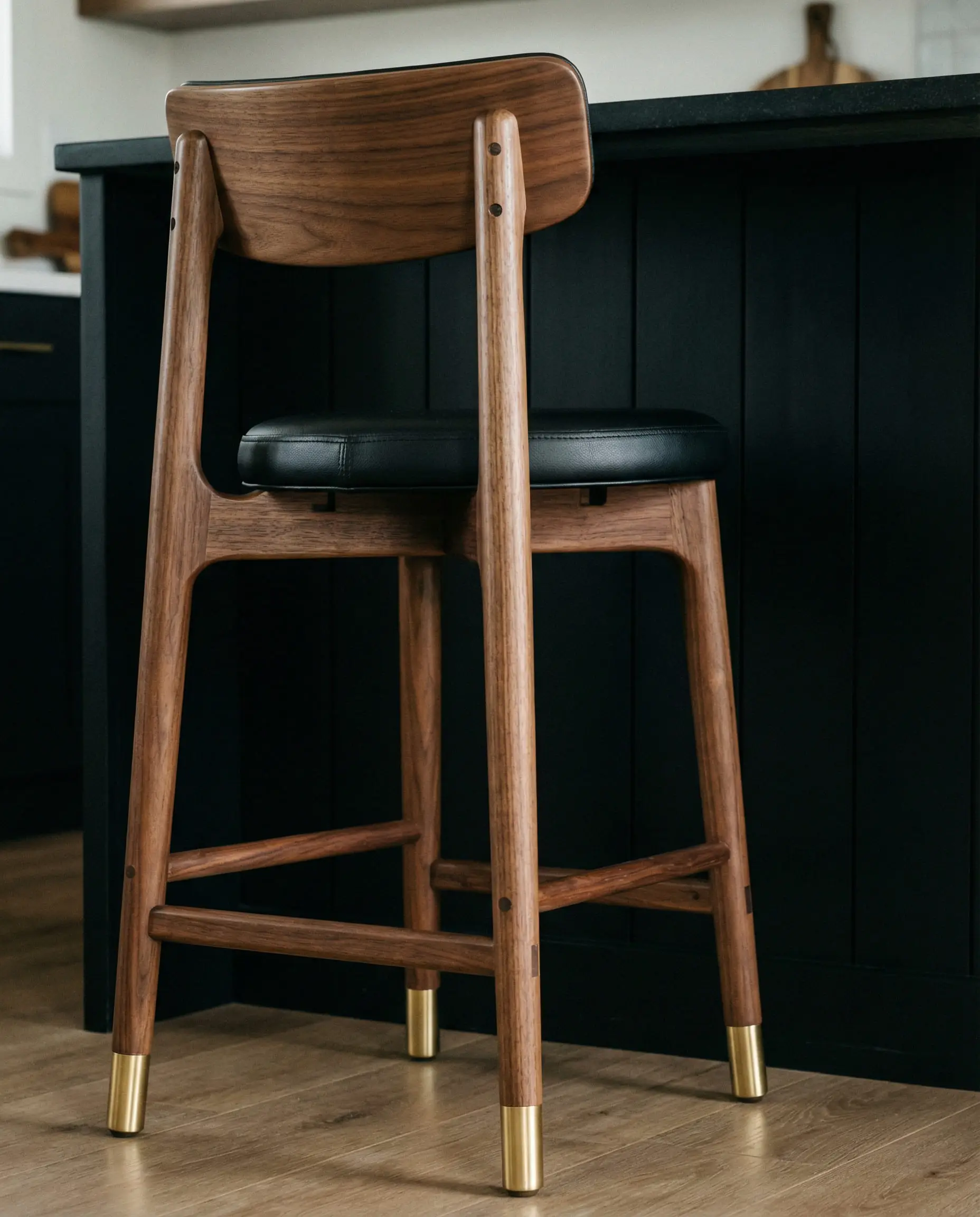 Detail of Mid-Century Modern walnut and black leather bar stool with brass capped feet.