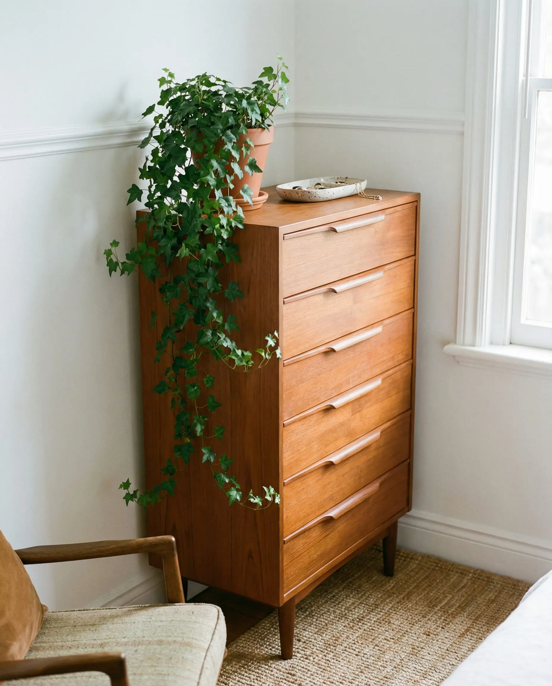 Tall vertical chest of drawers (tallboy) in a small bedroom corner with plants.