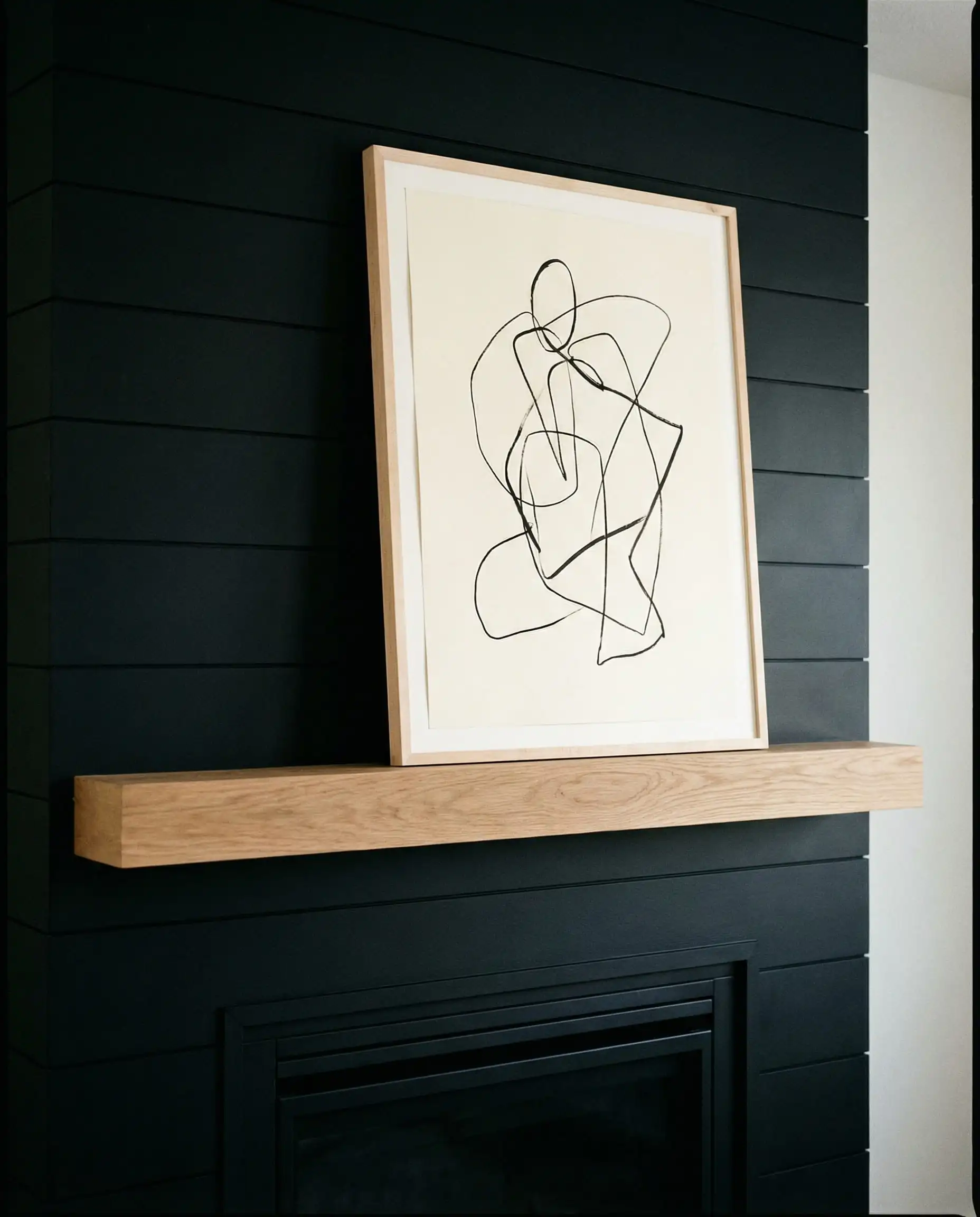 Black shiplap fireplace with an oak mantel styled with only a single abstract line drawing.