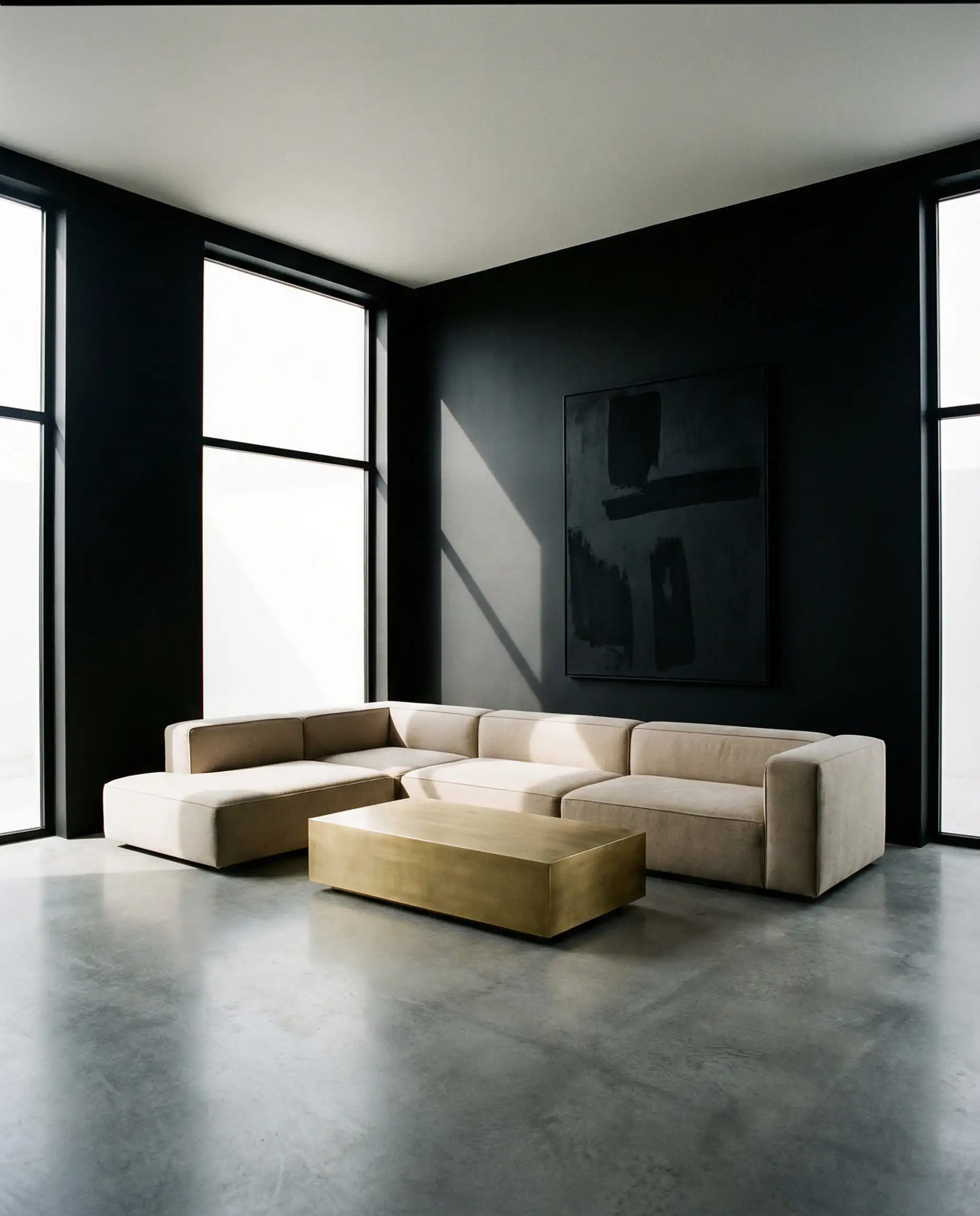 Ultra-minimalist living room with black walls, a beige sofa, and a simple gold coffee table.
