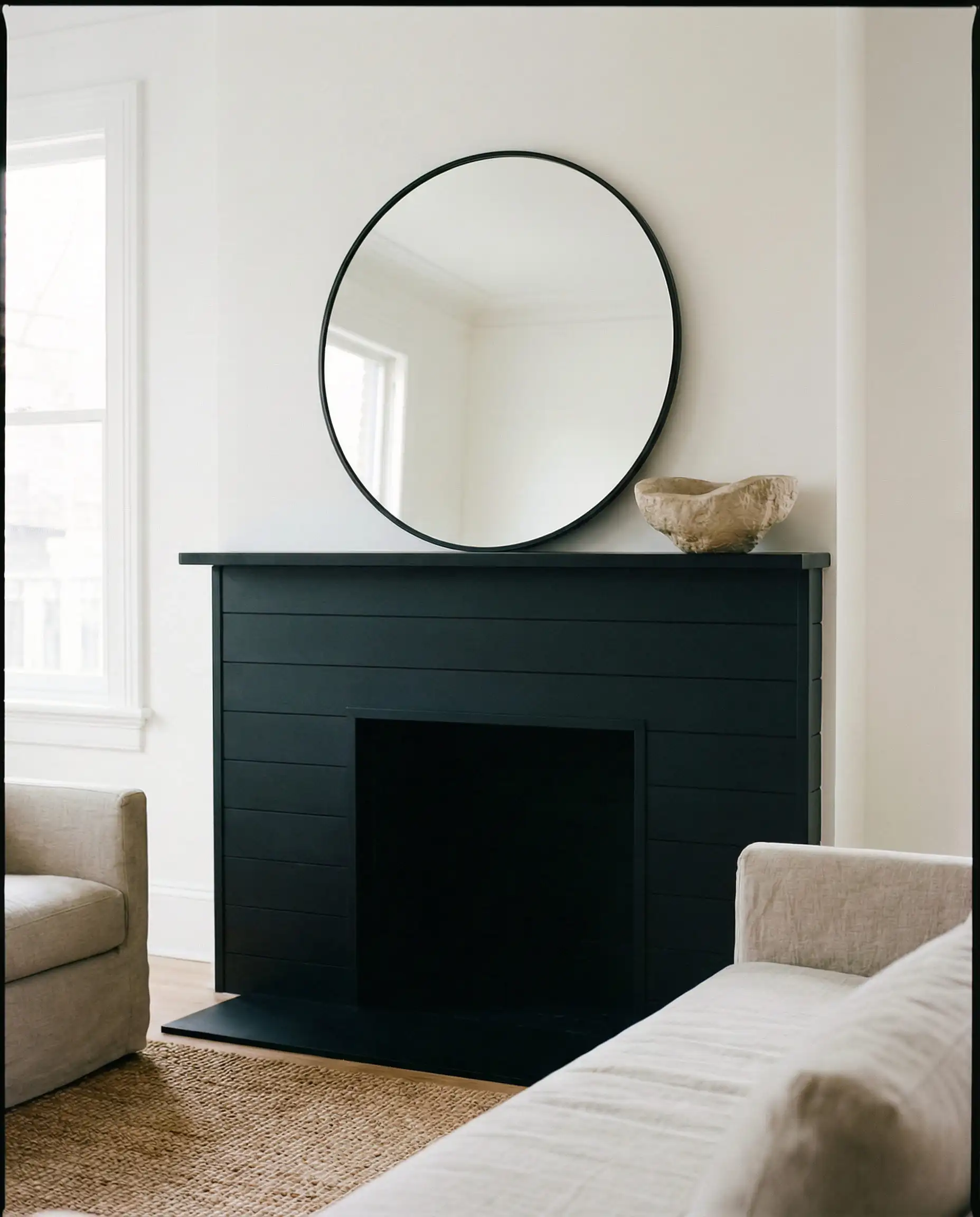 Simple styling with a round mirror and stone bowl on a black mantel.