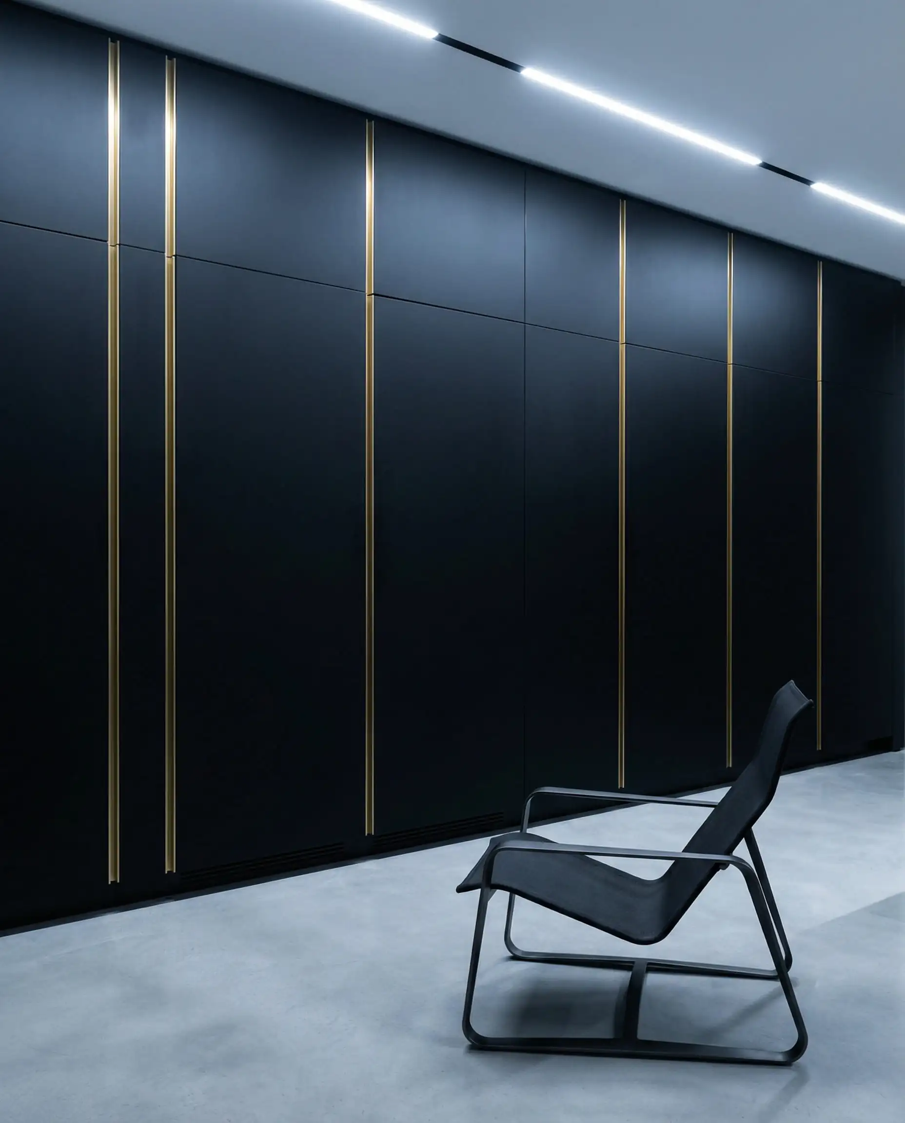 Ultra-minimalist kitchen wall with integrated black paneling hiding appliances, featuring thin vertical gold channel pulls.