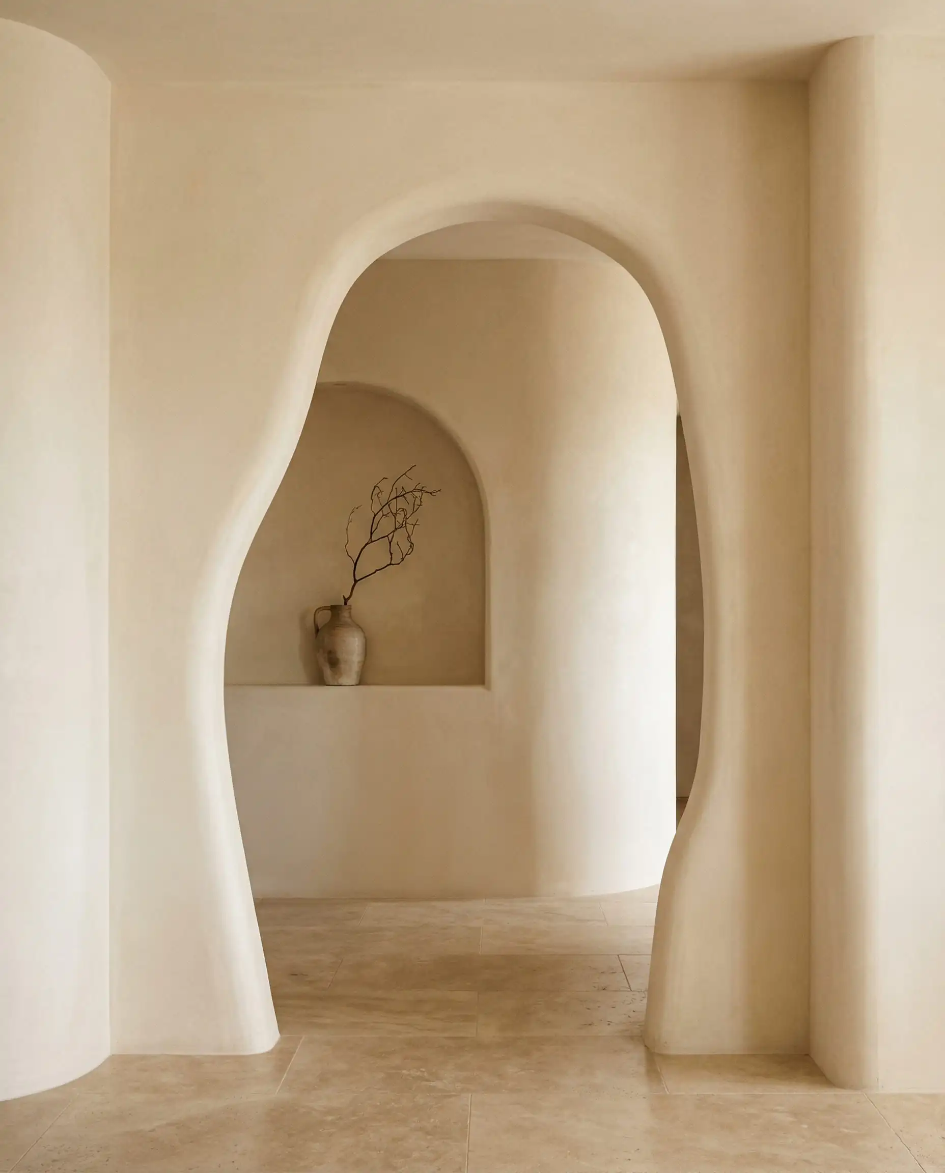 Modern minimalist hallway transition featuring a custom asymmetrical archway and a curved wall niche with a ceramic vase.