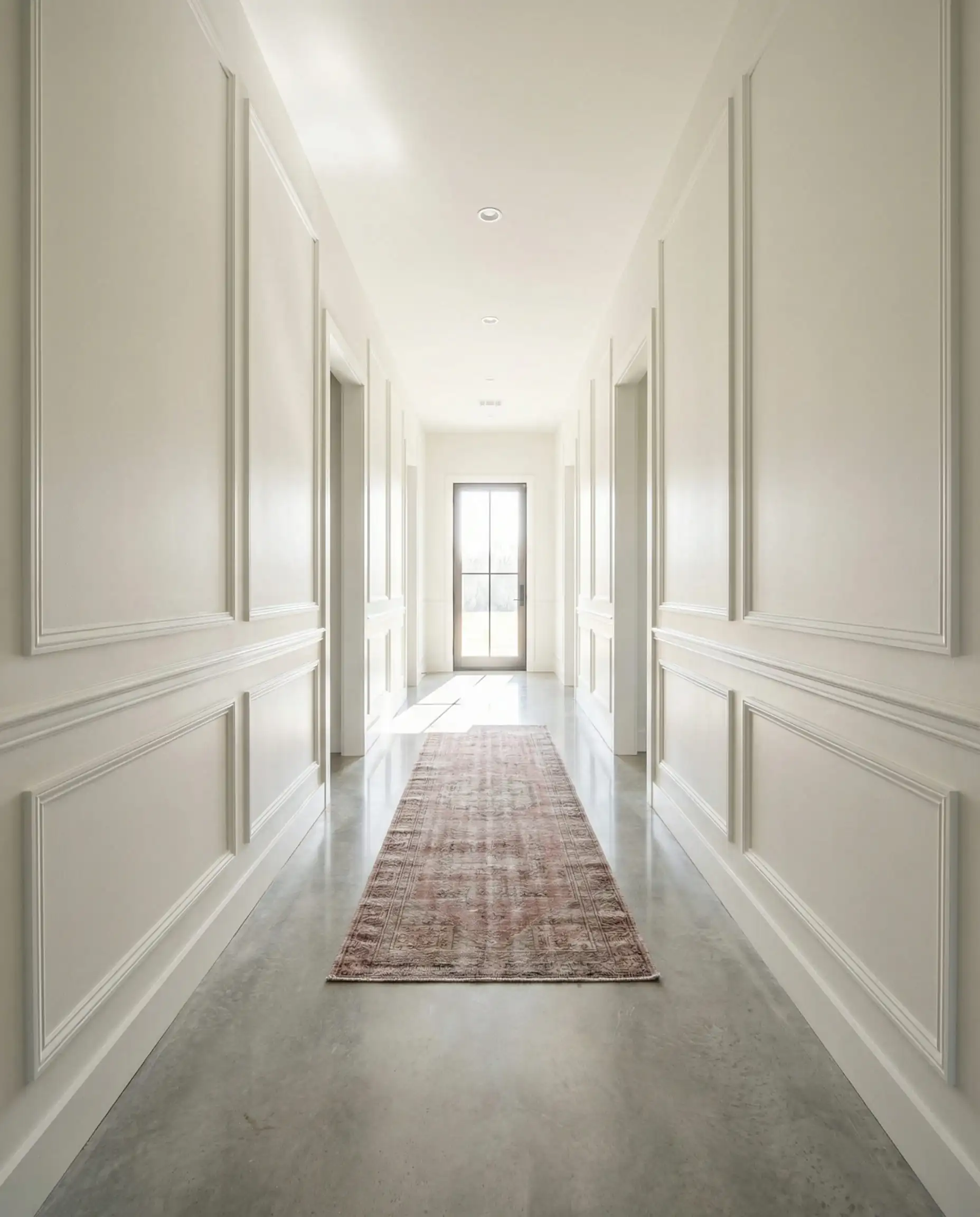 Long modern hallway with light gray polished concrete floors, Shoji White walls with wainscoting, and a vintage runner rug.