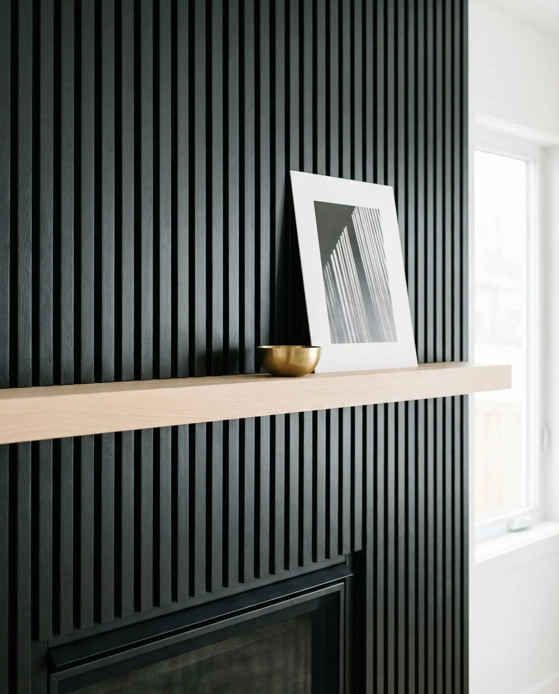 Minimalist black slat fireplace with a very thin, sleek floating blonde oak shelf.