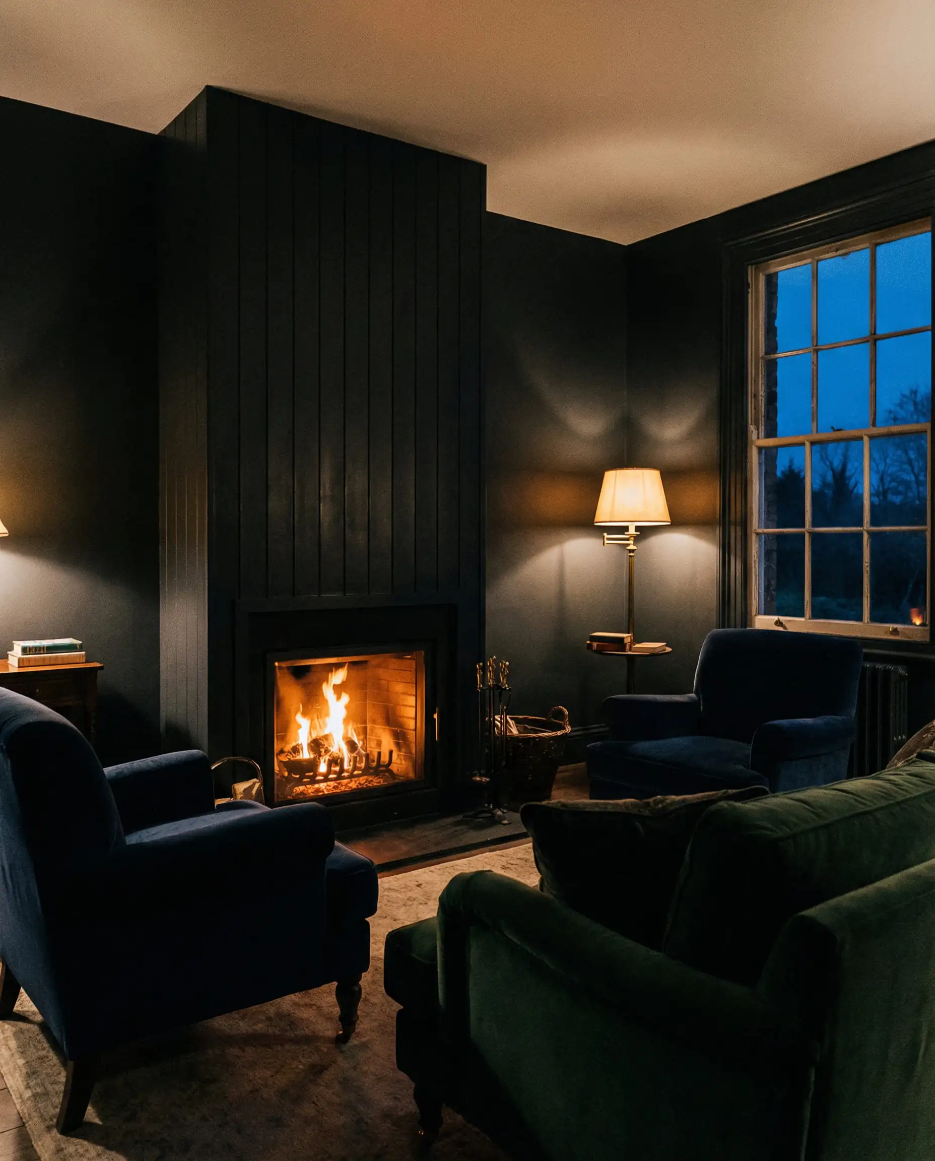 Dark and moody interior design with a black shiplap fireplace and velvet furniture illuminated by firelight.