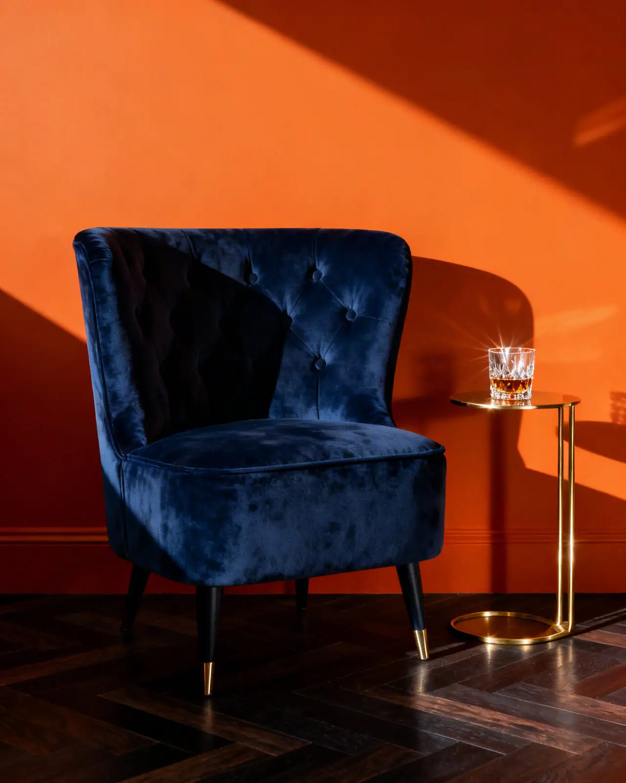 Detail shot of a deep navy blue velvet armchair placed against a smooth matte orange wall, showcasing high contrast design.