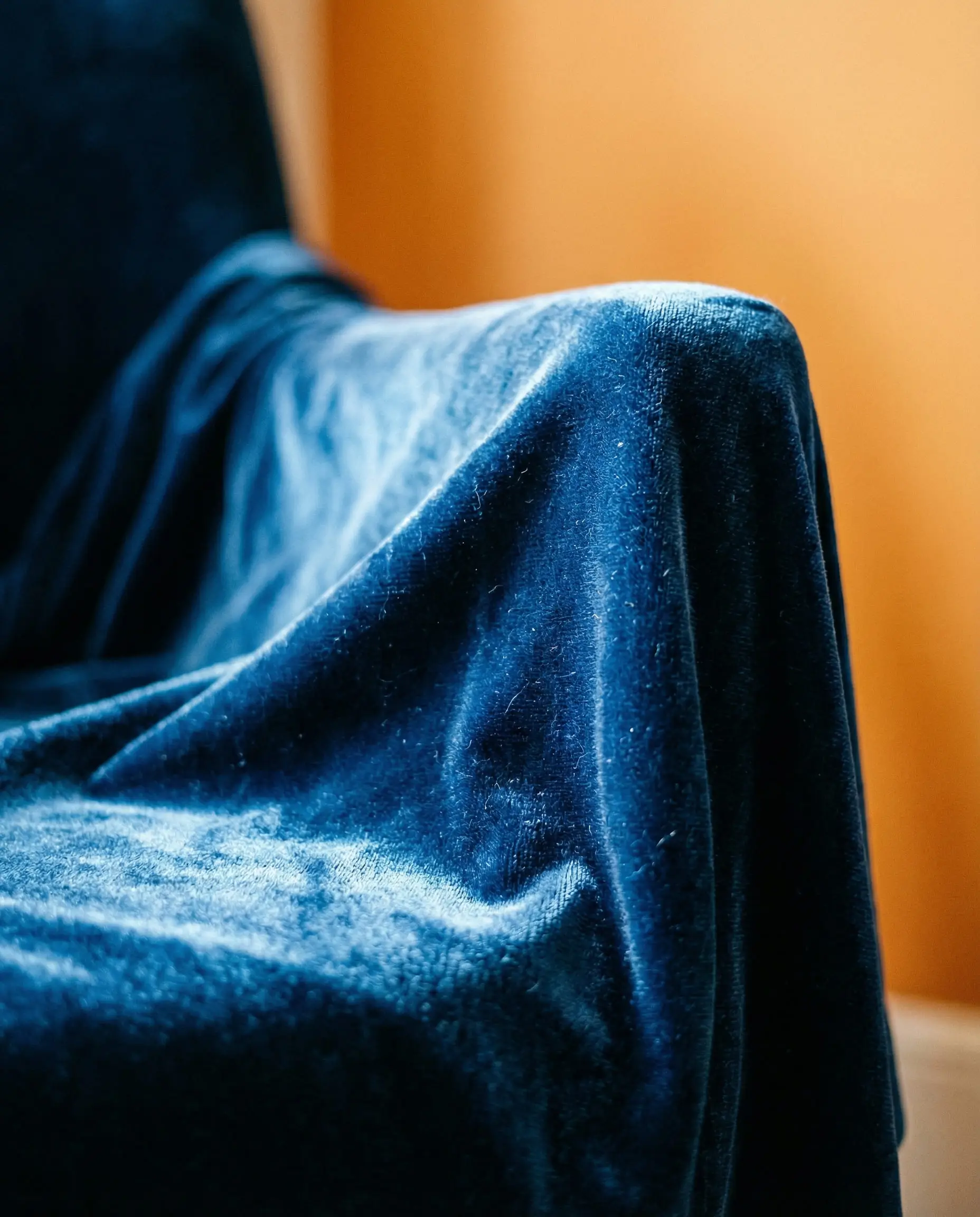 Macro detail shot of deep blue velvet fabric texture against a blurred orange wall background.