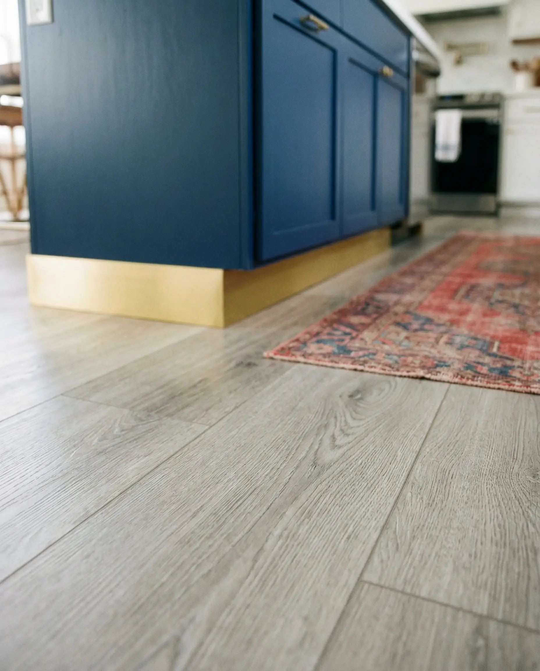 Low angle shot of a navy blue kitchen island with a brass kickplate on light gray wood flooring.