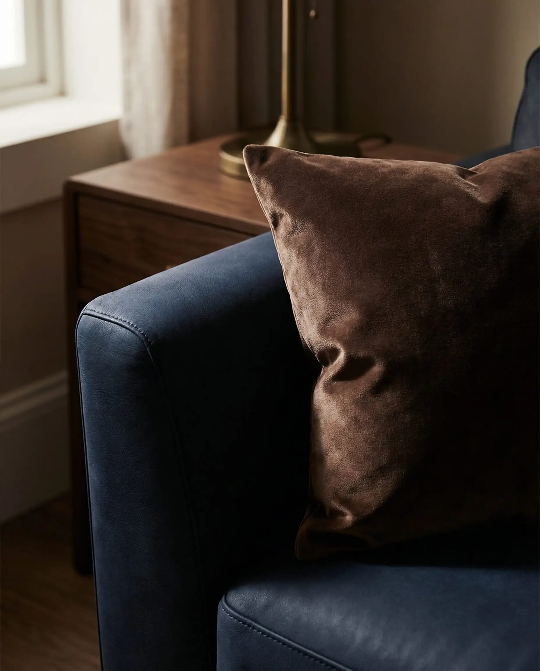 Close-up detail of a navy blue leather couch styled with a rich chocolate brown velvet throw pillow to create a moody color palette.