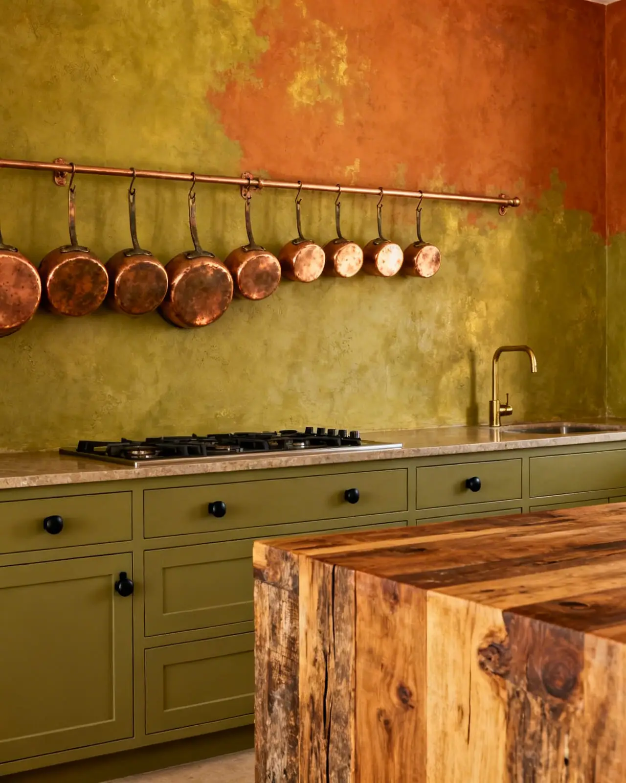 Rustic farmhouse kitchen with olive green lower cabinets, terracotta lime wash walls, and hanging copper cookware.