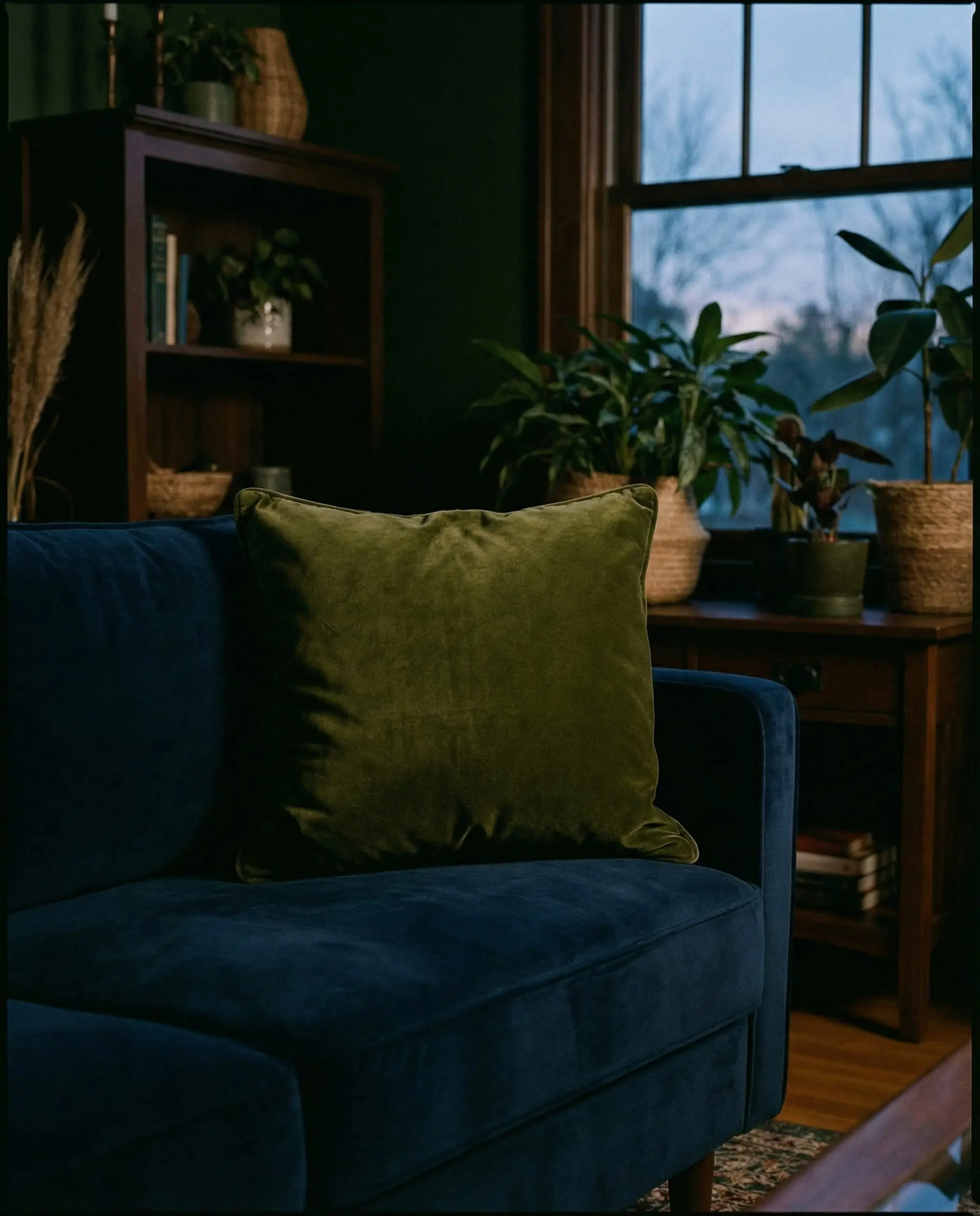 Deep olive green velvet pillow on a navy blue couch.