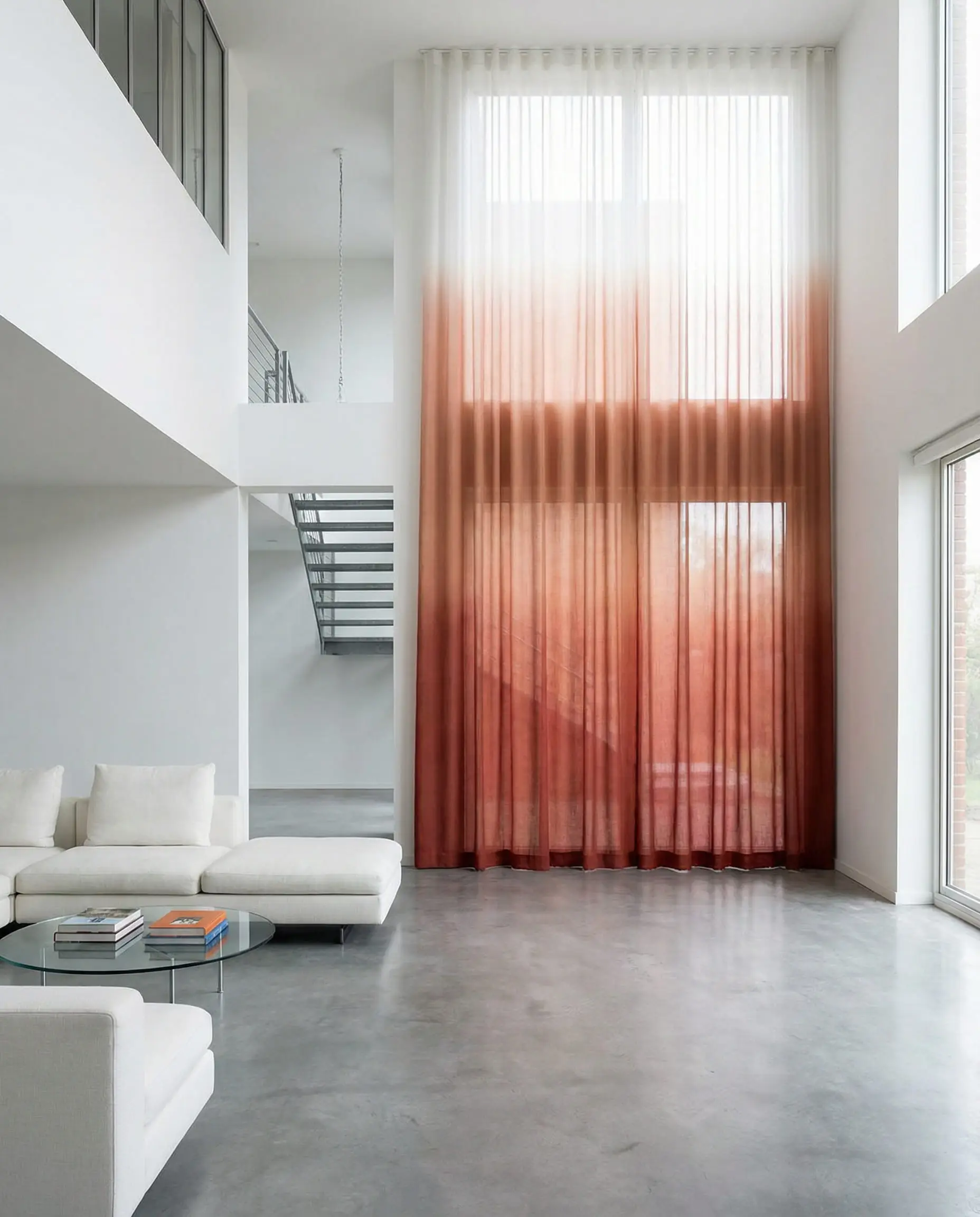 Floor-to-ceiling ombre curtains fading from deep rust red at the bottom to white at the top in a modern loft.