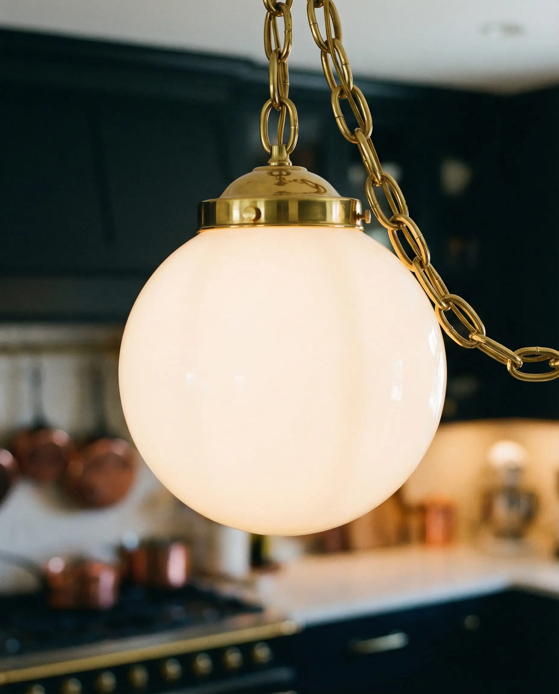 Close-up of a single opal glass globe pendant with a heavy brass chain.