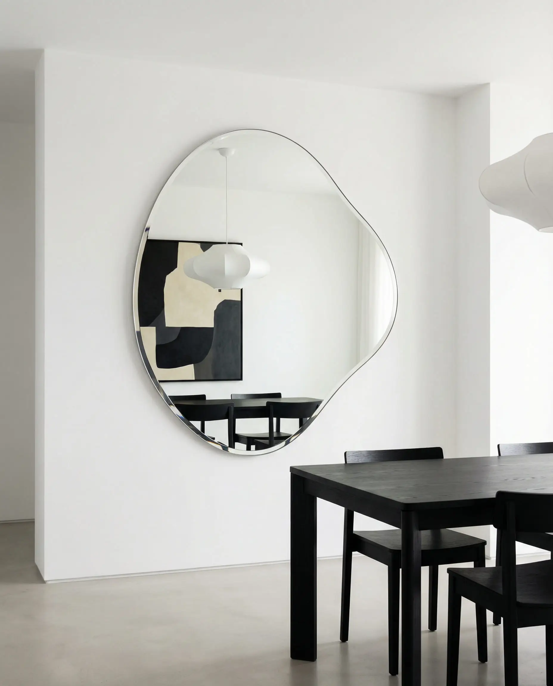 Minimalist dining room featuring a large, frameless mirror in an asymmetrical organic pebble shape.