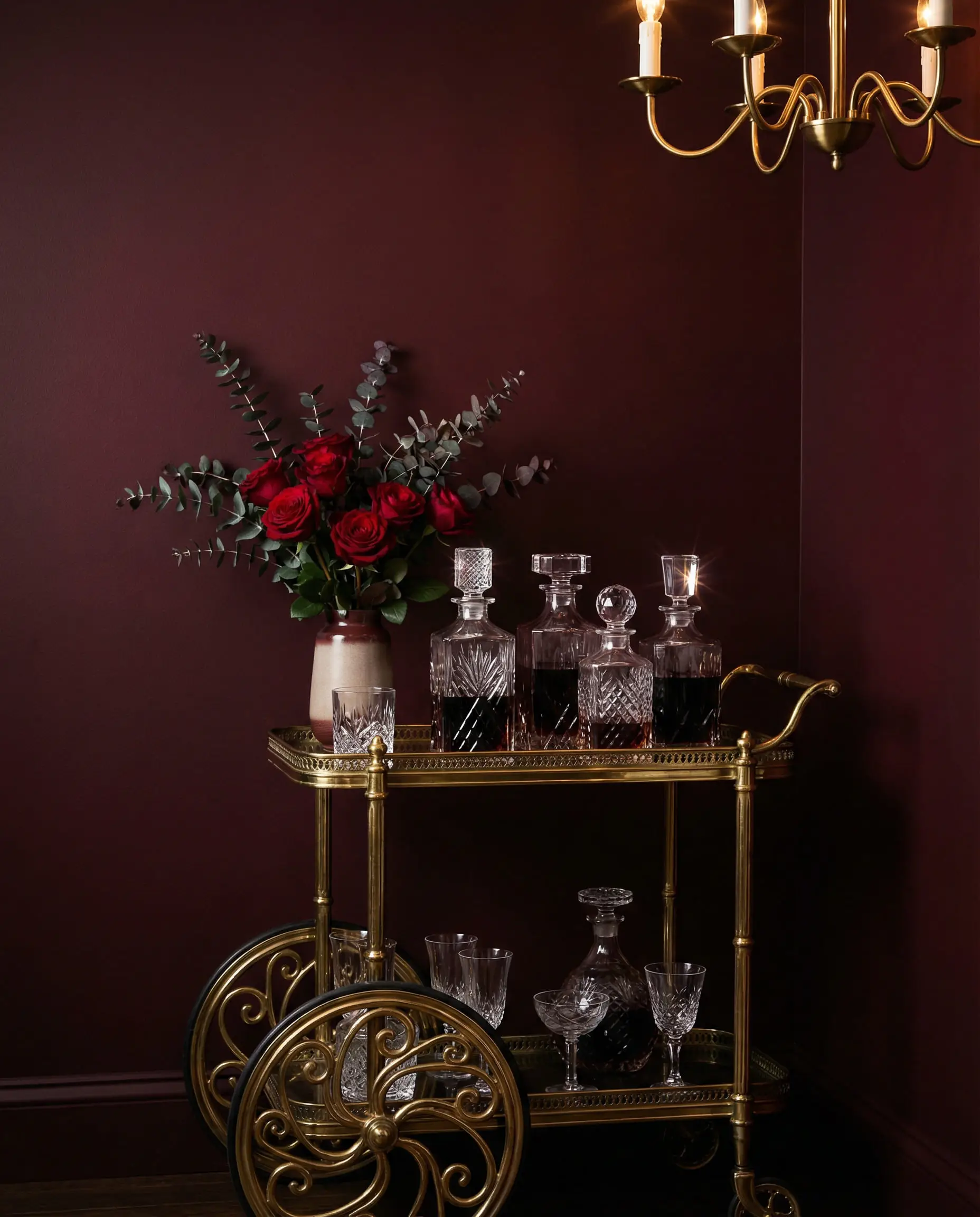 Dramatic dining room featuring deep oxblood red walls and a vintage brass bar cart with crystal decanters.