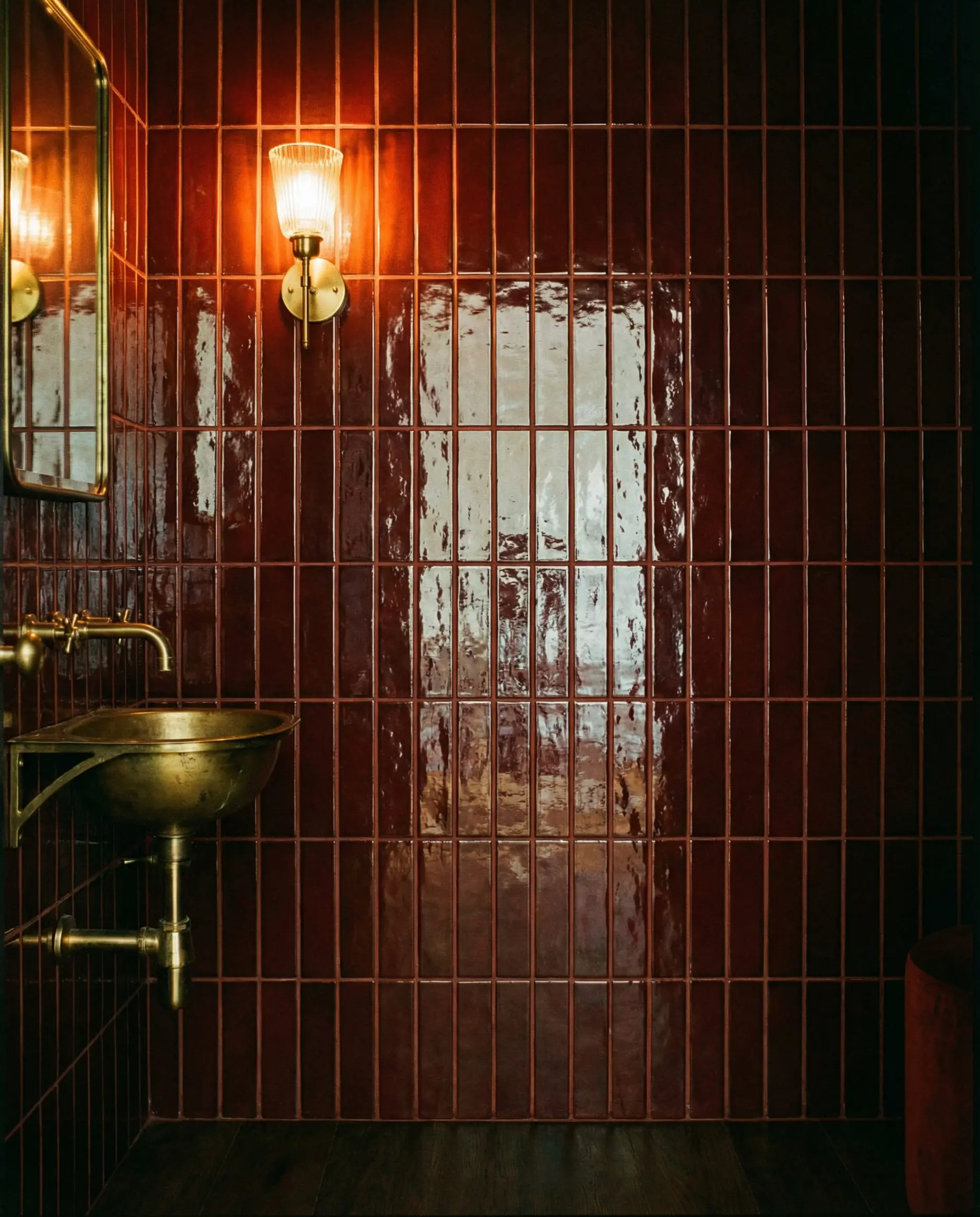 Dramatic powder room with vertical stacked glossy oxblood red tiles and brass accents.