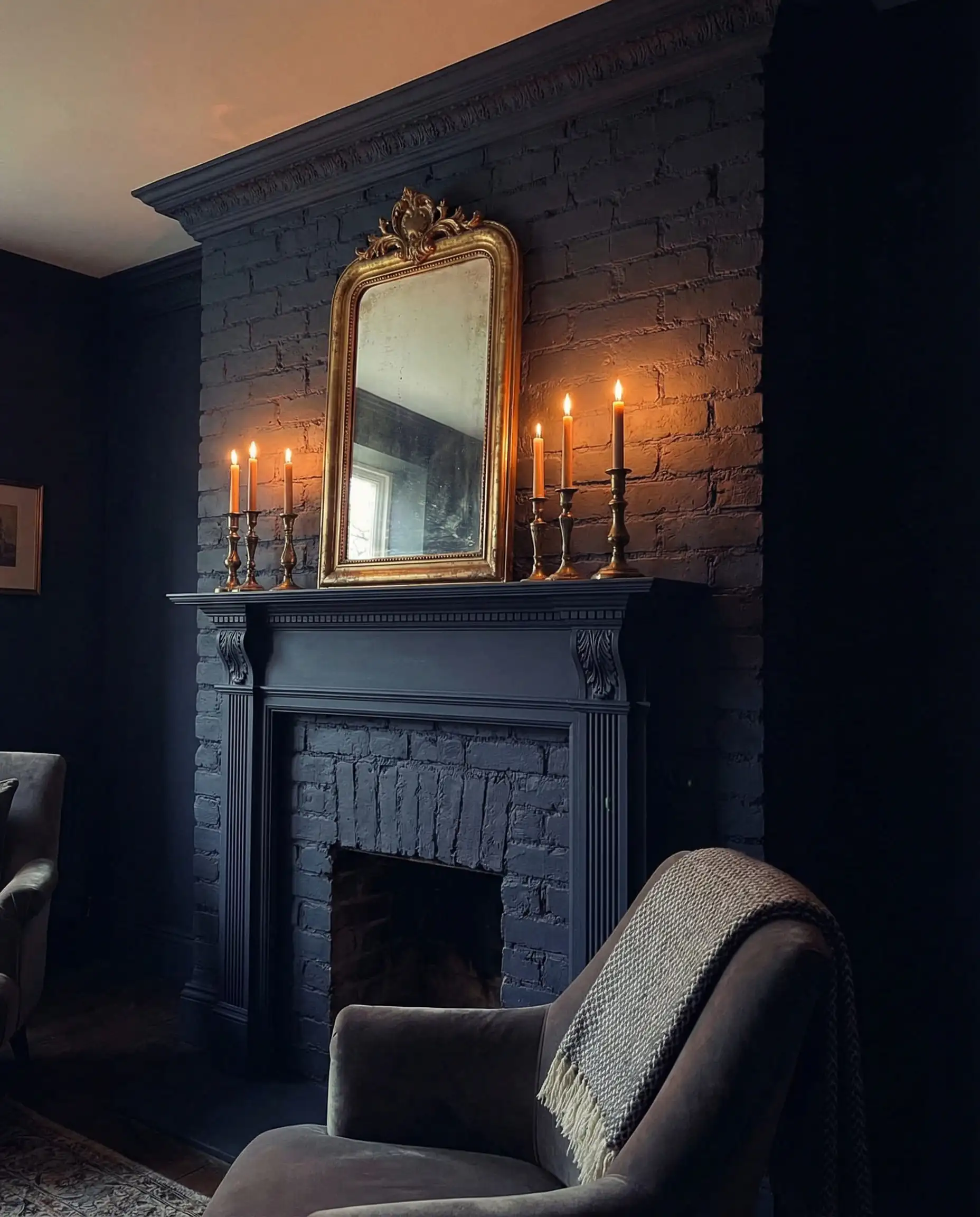 Moody interior with a fireplace surround and wood mantel painted the same dark charcoal color for a monochromatic look.