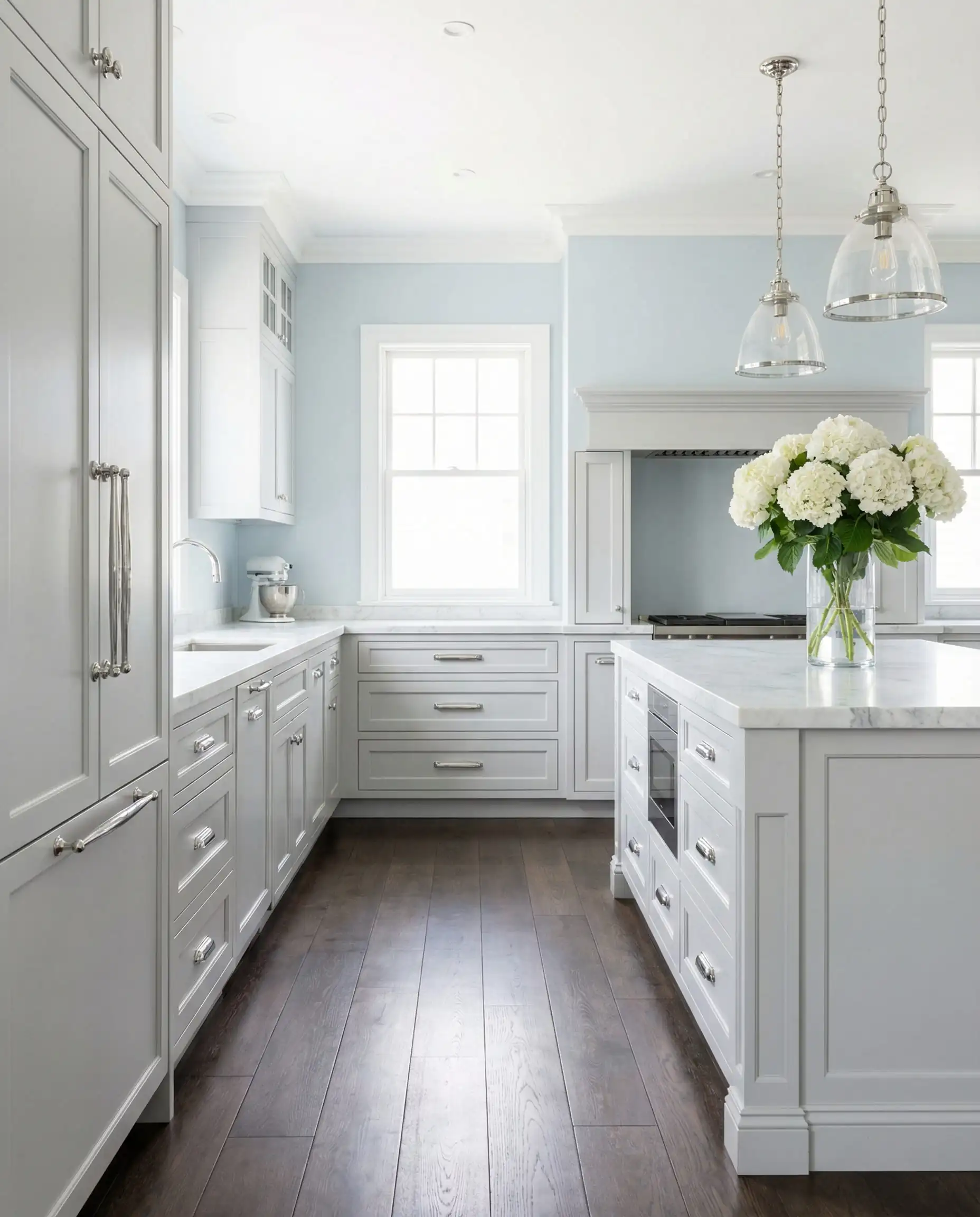 Bright Hamptons-style kitchen with light gray cabinets, misty blue walls, and white hydrangeas.